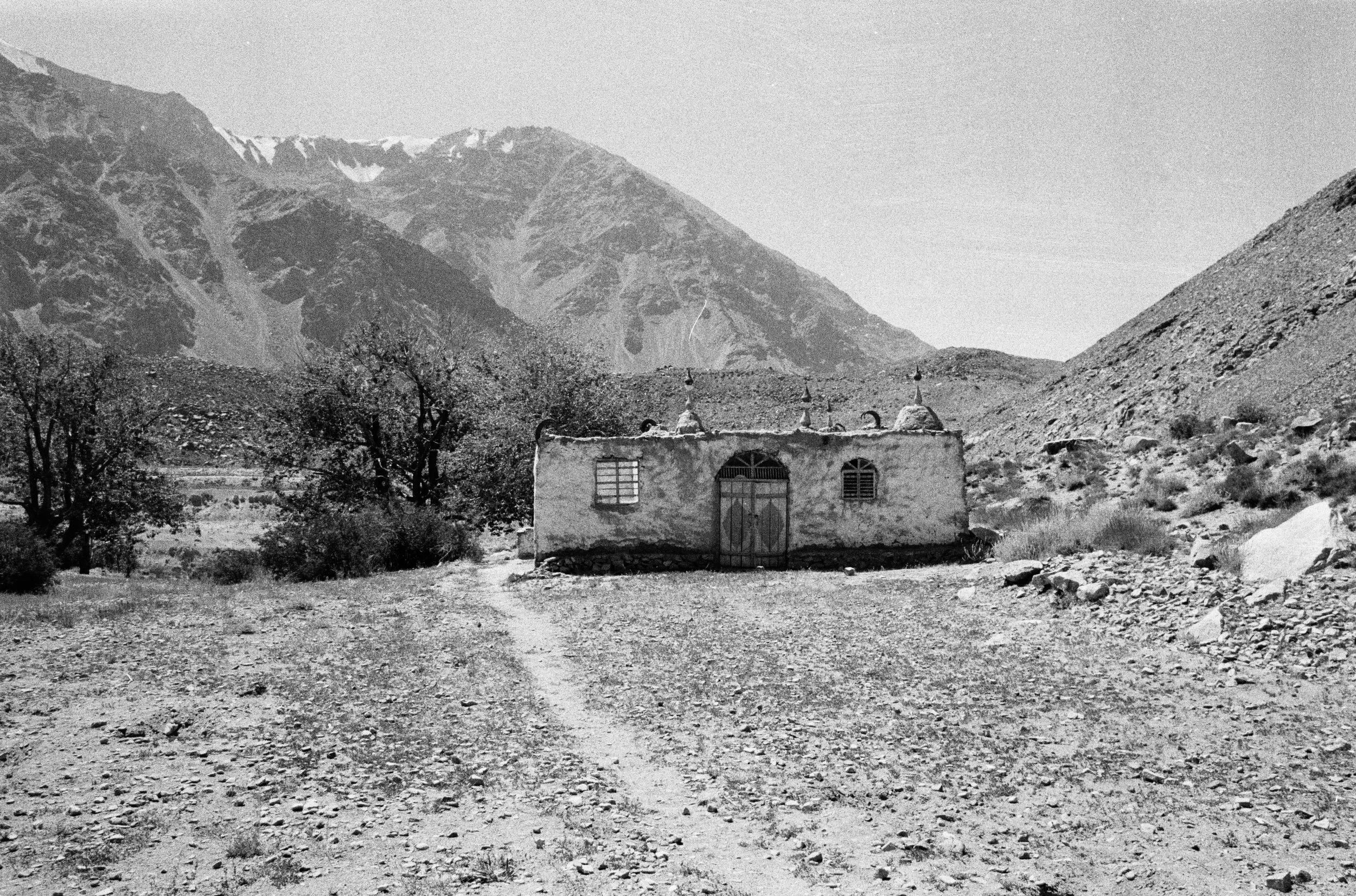 Une maison en adobe avec des cheminées et des fenêtres dans un paysage montagneux aride en noir et blanc.