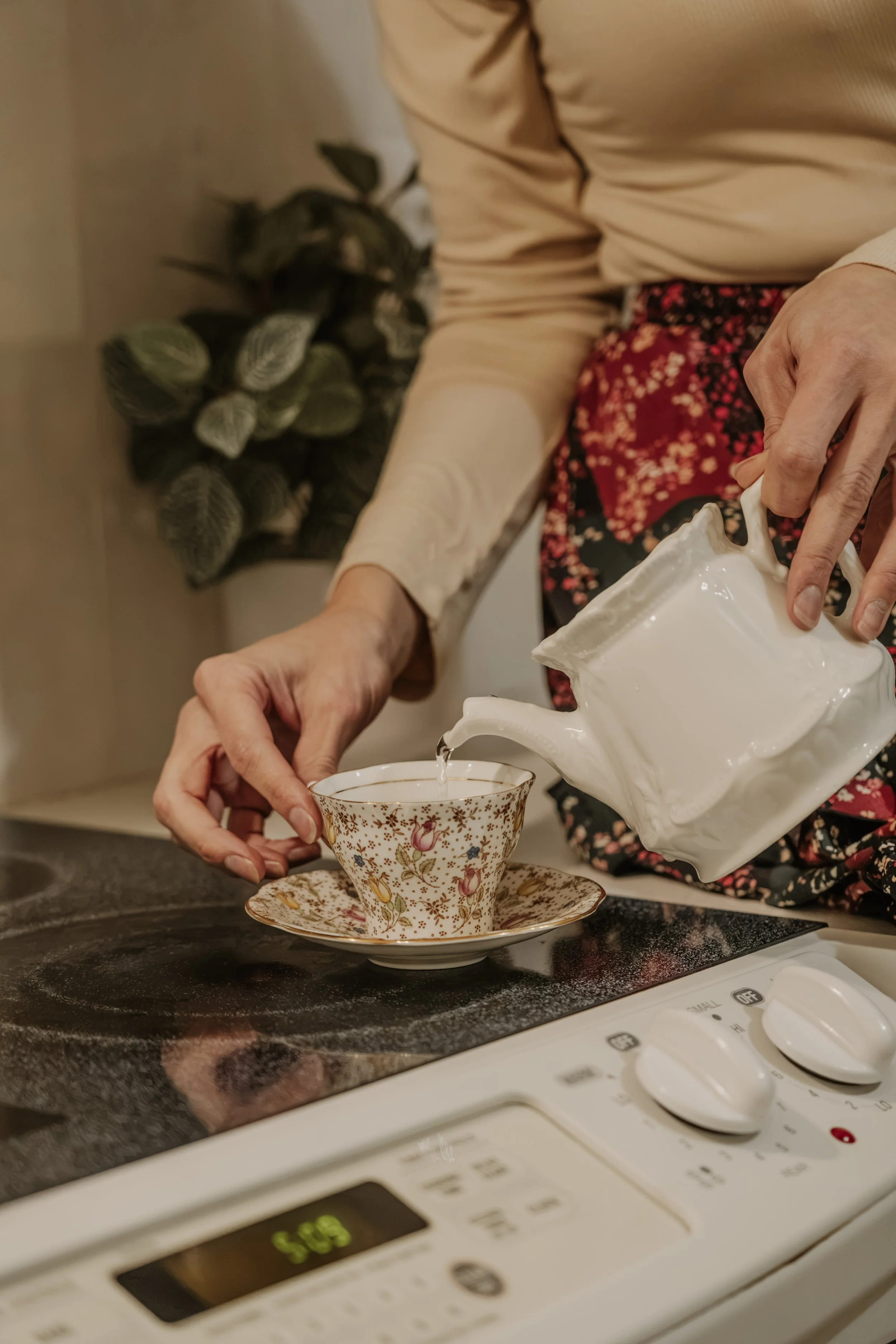 Pouring tea from a white teapot into a floral teacup