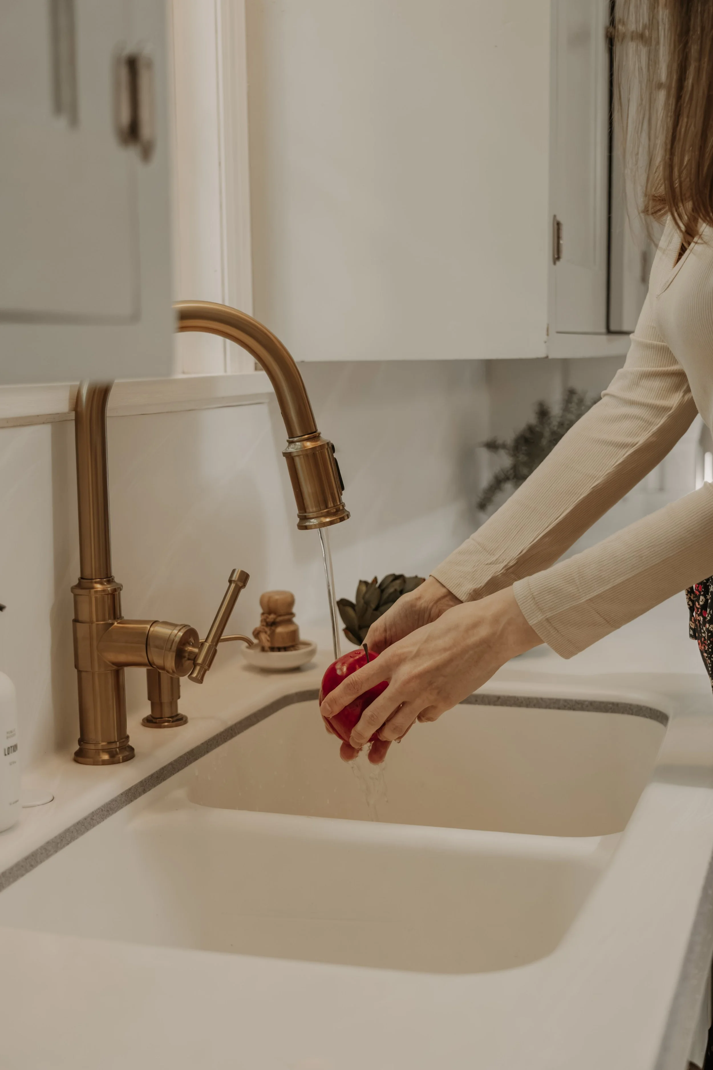 Rinsing a red apple under a brass kitchen faucet