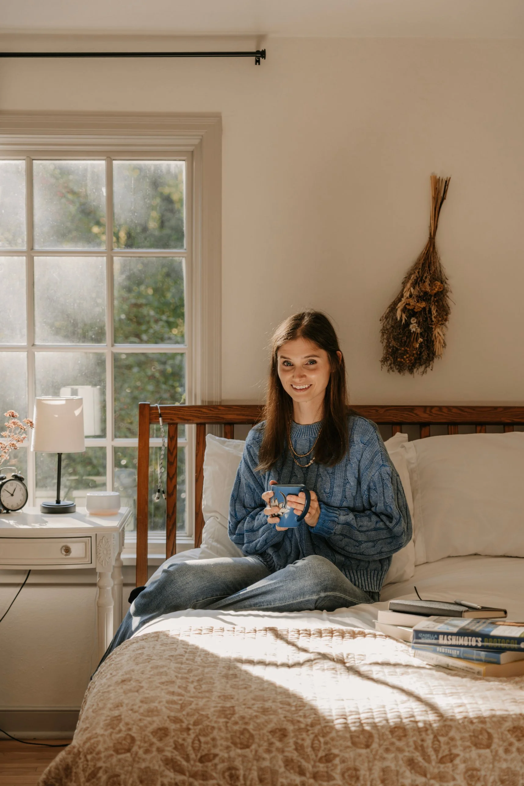 Cassandra sitting on a bed with a cup of tea in a cozy home