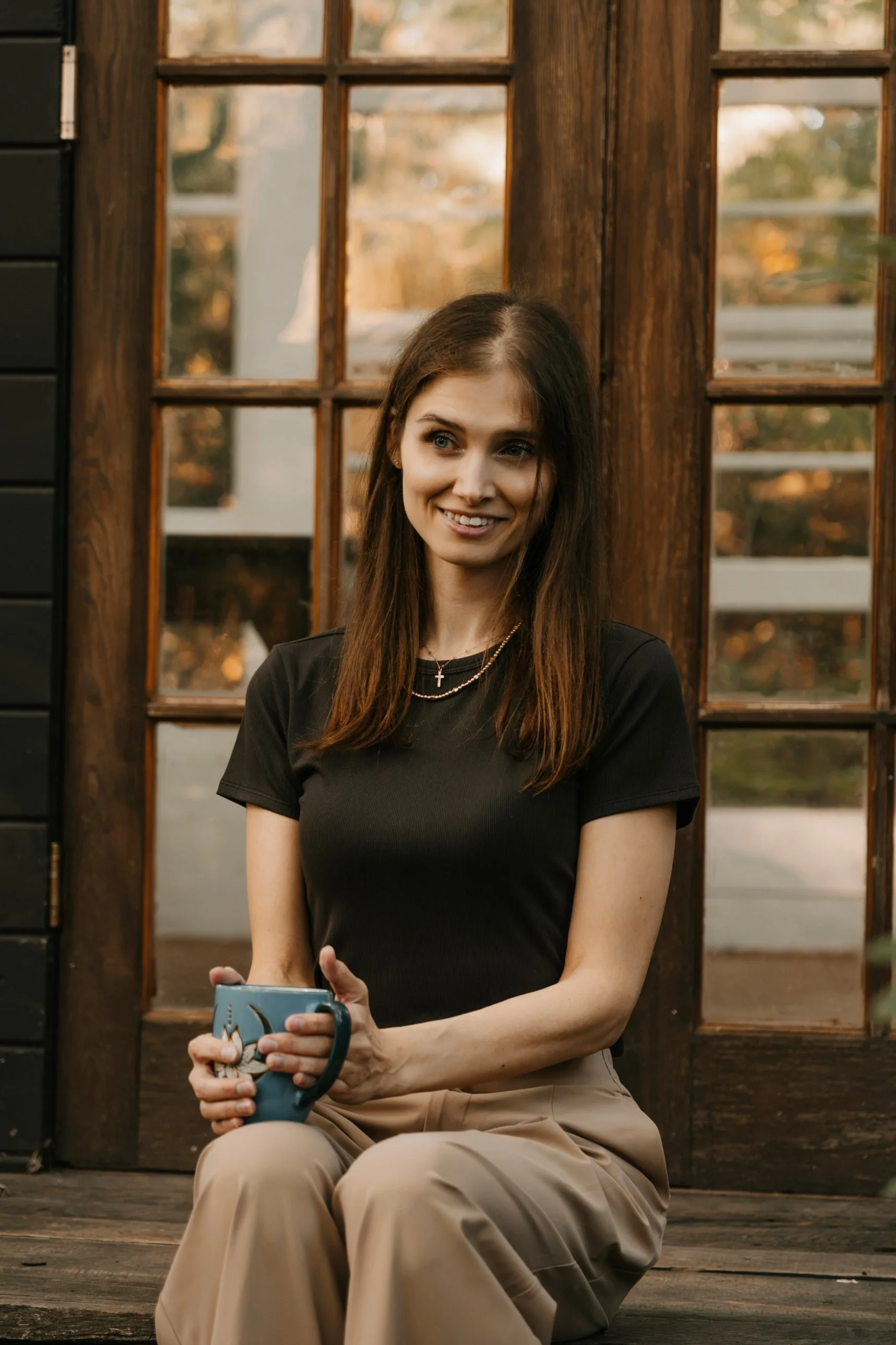 Cassandra Pedersen, RD, smiling and holding a mug of tea outside a wooden cabin door