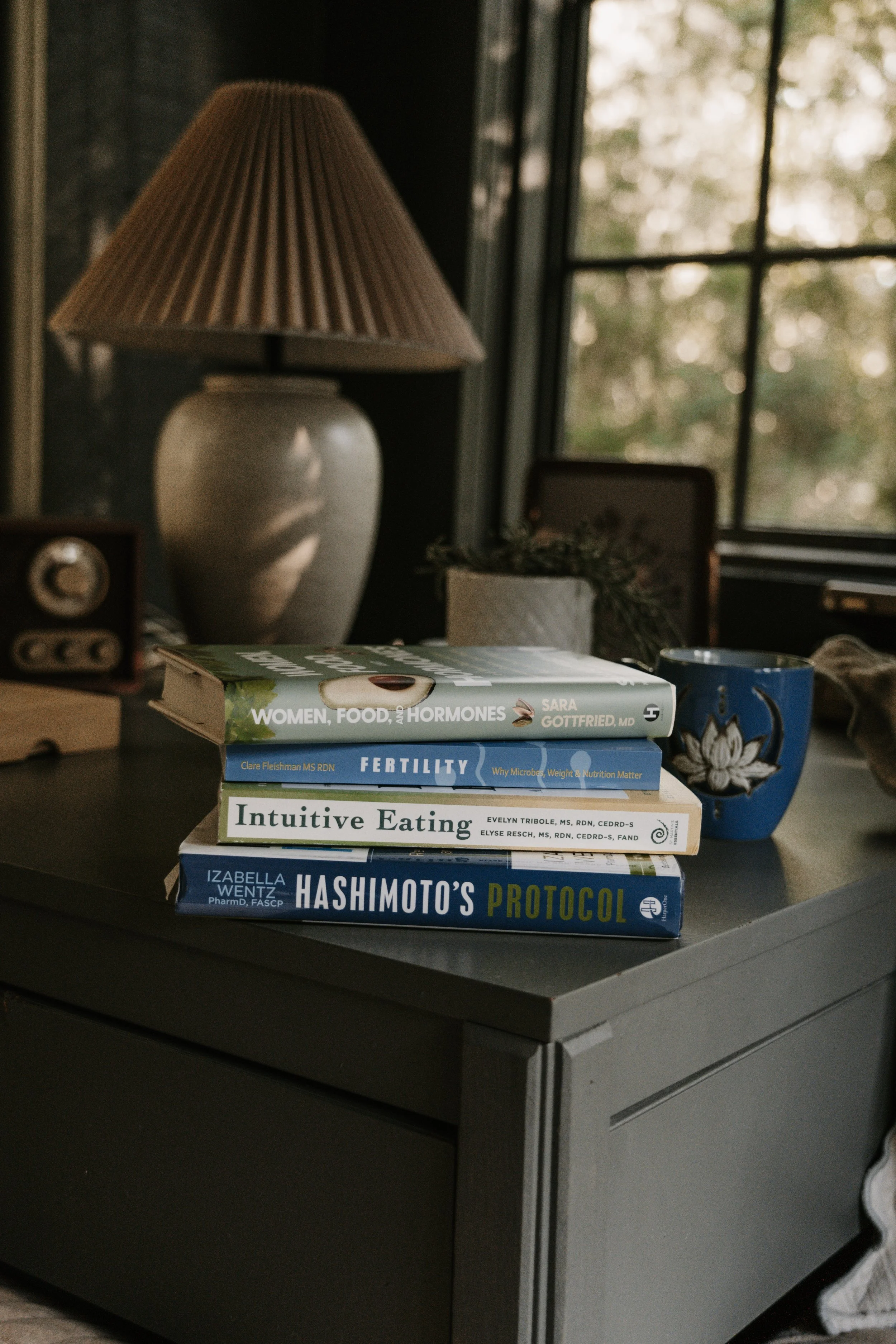 Stack of nutrition and health books beside a blue holistic mug