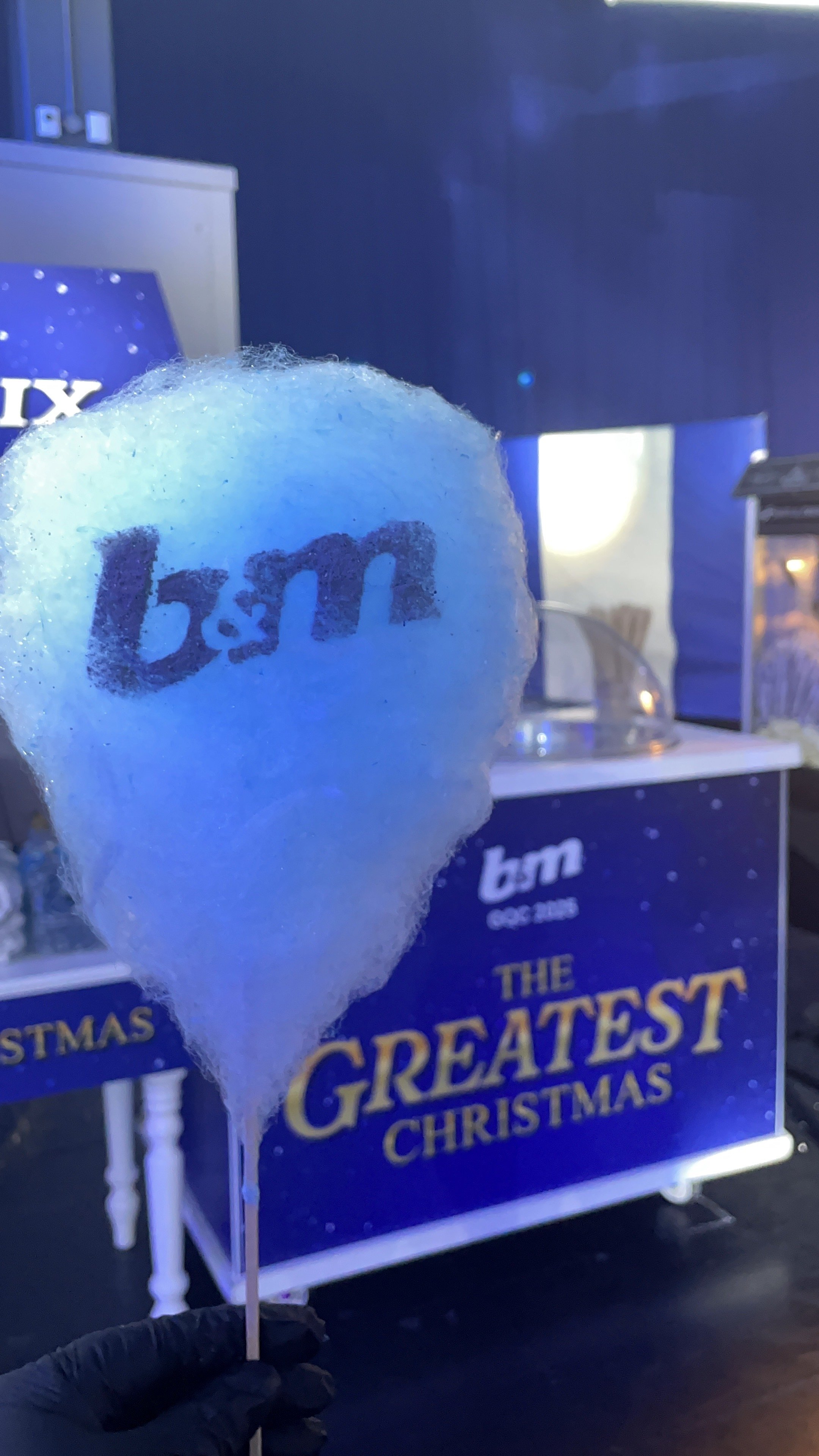 Cotton candy with 'L & M' written on it, held in front of a Christmas display promoting 'The Greatest Christmas' show.