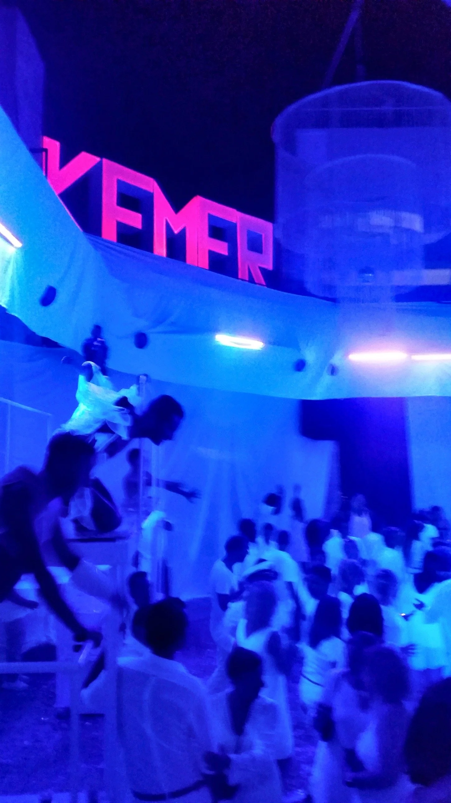 Une soirée au Club Med Kemer sous des lumières bleues, avec l’enseigne KEMER au-dessus de la foule et un artiste en plein saut