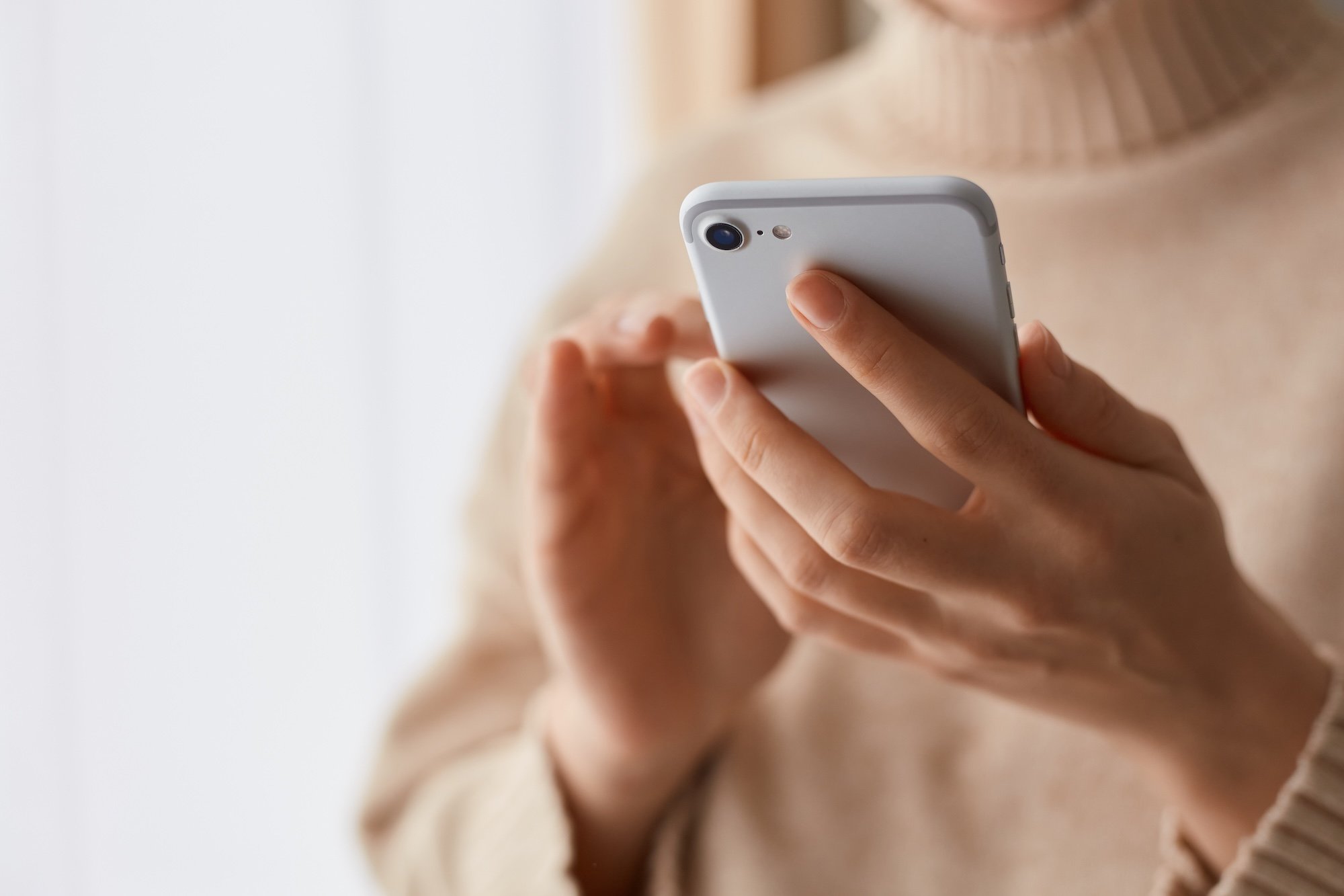 Person holding and using a smartphone with a white back, wearing a beige sweater.