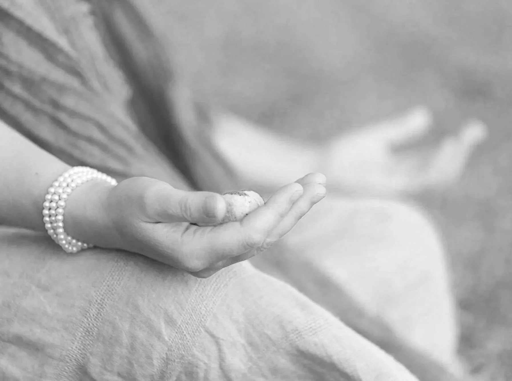 A person sits cross-legged with open palms resting on their knees, wearing a beaded bracelet.