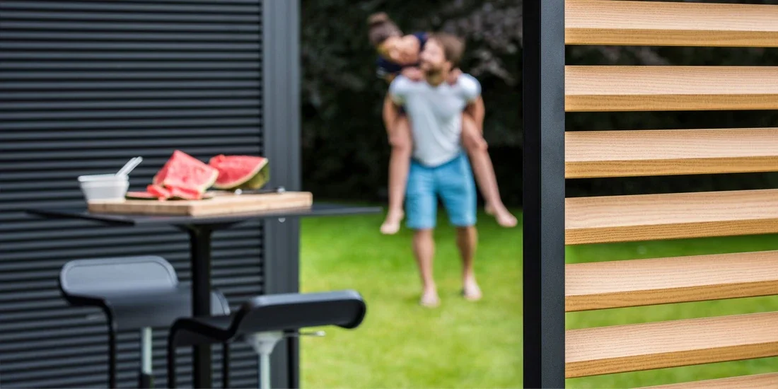 Person giving piggyback ride to another person in a backyard, with a table of watermelon slices and a bowl in the foreground.