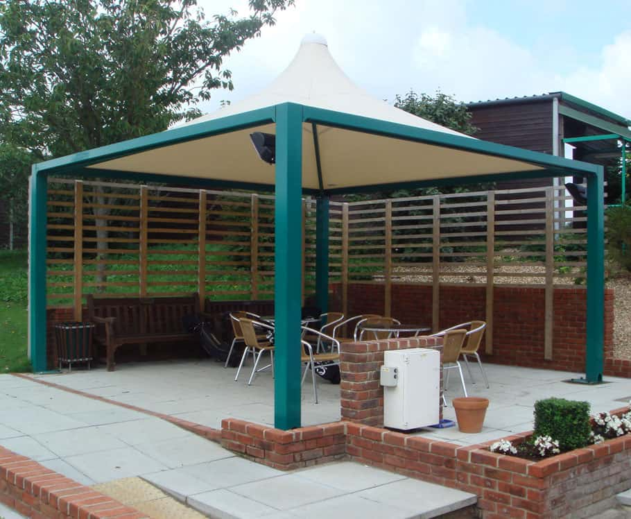 Outdoor patio area with a canopy, chairs, benches, plants, and a fence.
