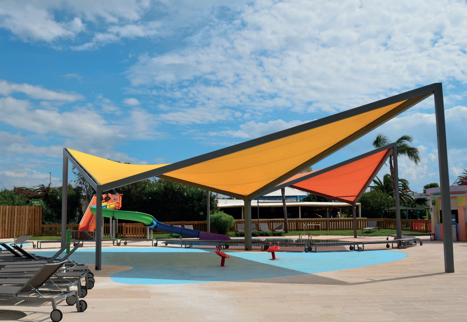 Empty outdoor water park with colorful shade structures, water slide, lounge chairs, and a clear blue sky.