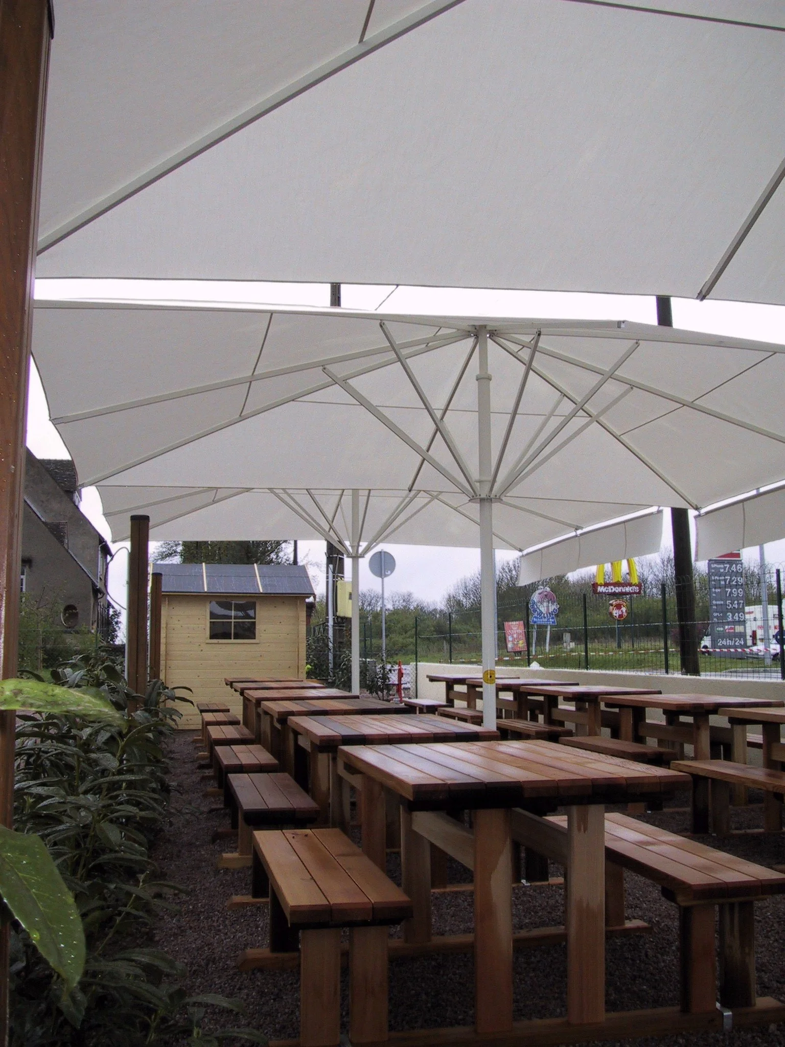 Outdoor dining area with wooden picnic tables and large white umbrellas for shade.