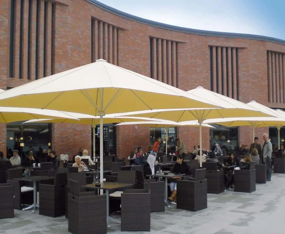 Outdoor patio of a restaurant with yellow umbrellas, black tables and chairs, and people dining against a brick building.