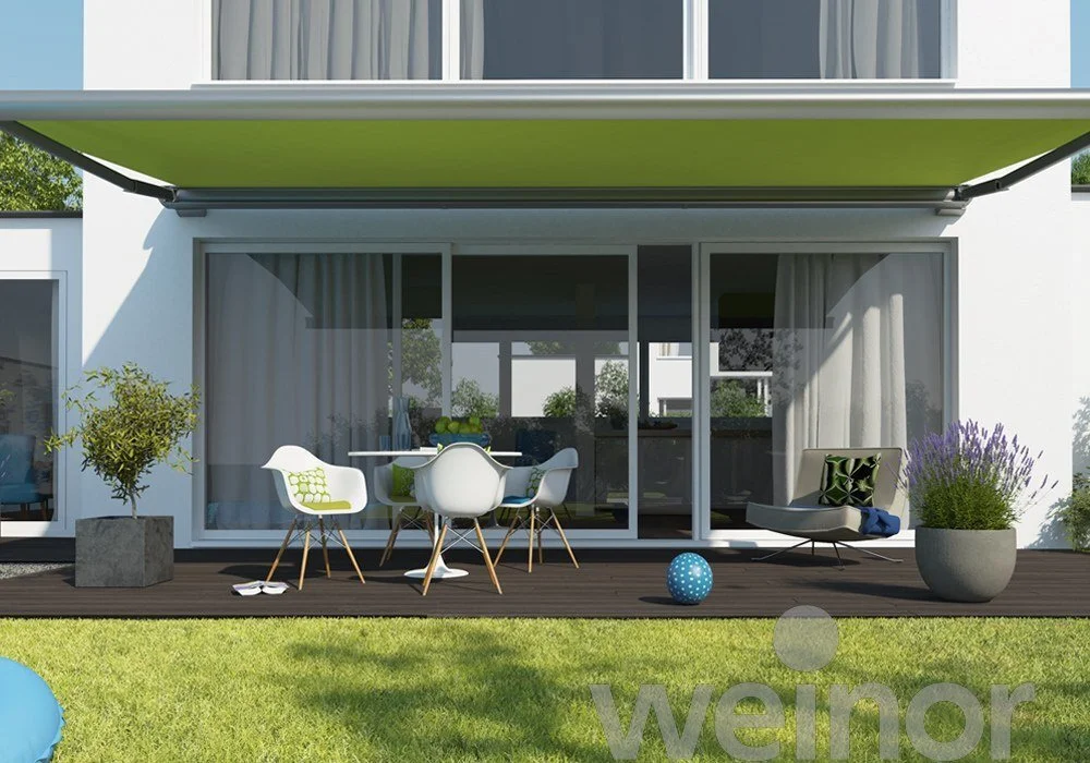 Modern balcony with outdoor furniture, potted plants, and a view of the house interior through glass sliding doors.