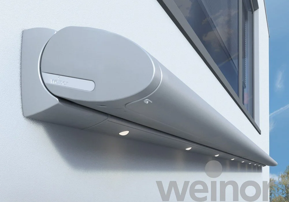 Modern exterior wall-mounted air conditioning unit below a large window on a white building.