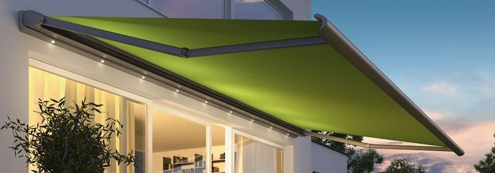 Green retractable awning extend over a patio of a modern home at dusk.