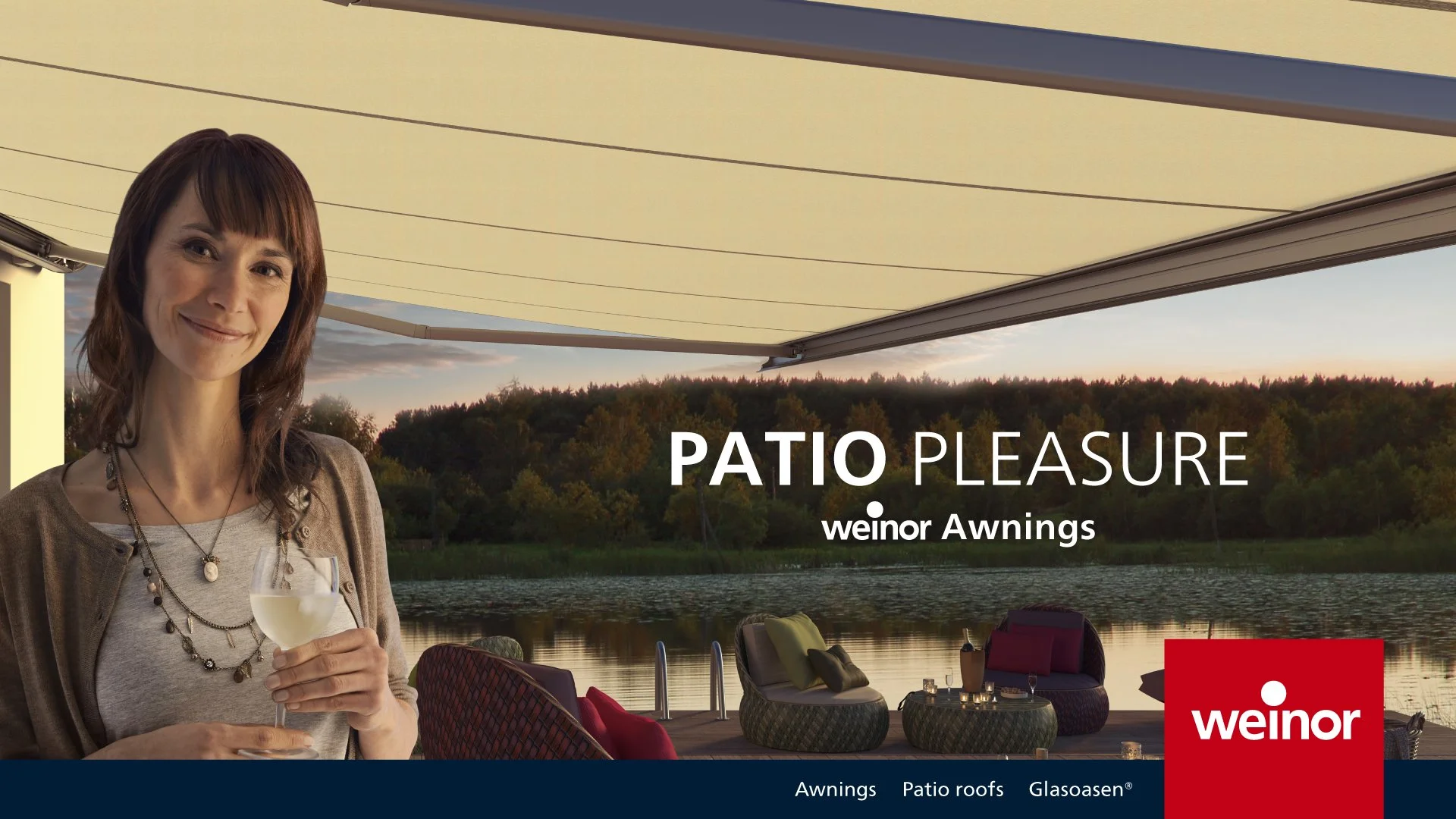 Woman holding a glass of white wine on a patio with a view of a lake, trees, and a sunset sky, featuring Weinor awnings.