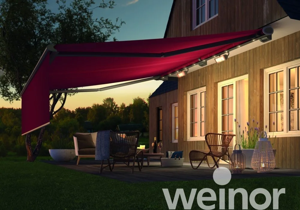 Outdoor patio at dusk with seating, lanterns, and a red retractable awning attached to a wooden house.