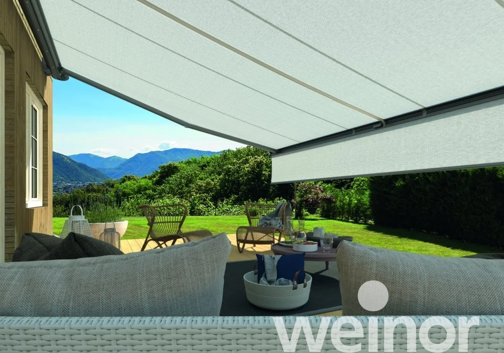 Outdoor patio with seating area, wicker sofas and chairs, a table with food and drinks, and a view of green mountains and blue sky in the background