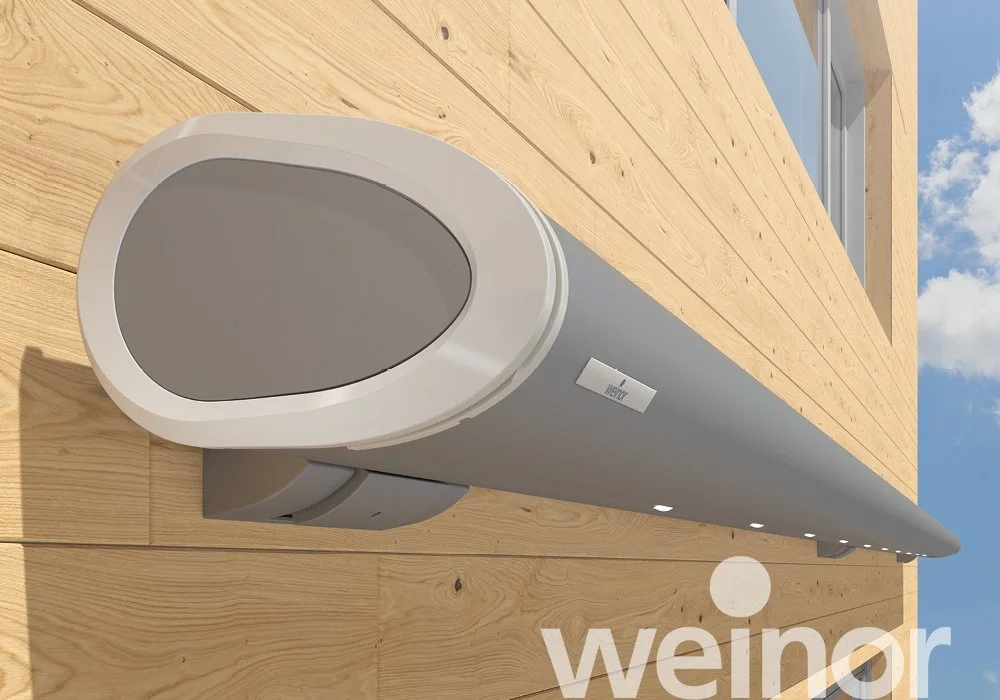 A sleek, modern outdoor speaker mounted on a wooden wall with clear blue sky and clouds in the background.