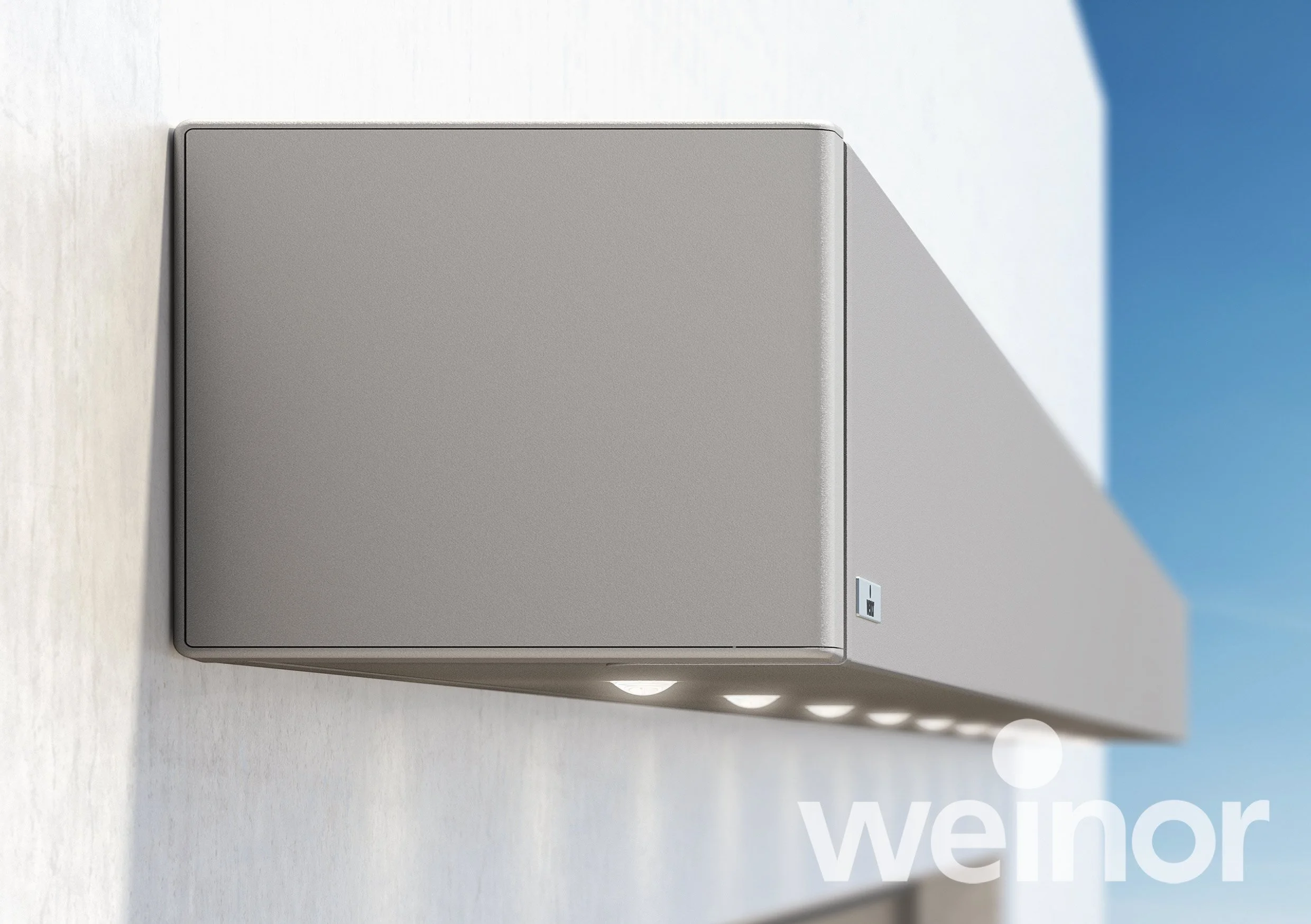 Modern gray outdoor wall-mounted light fixture with multiple lights and a small control panel, attached to a light-colored wall with a blue sky background.