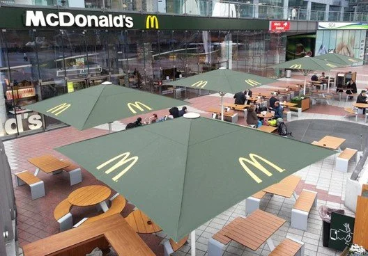 Outdoor seating area with tables, benches, and large green umbrellas with yellow McDonald's logos outside a McDonald's restaurant.