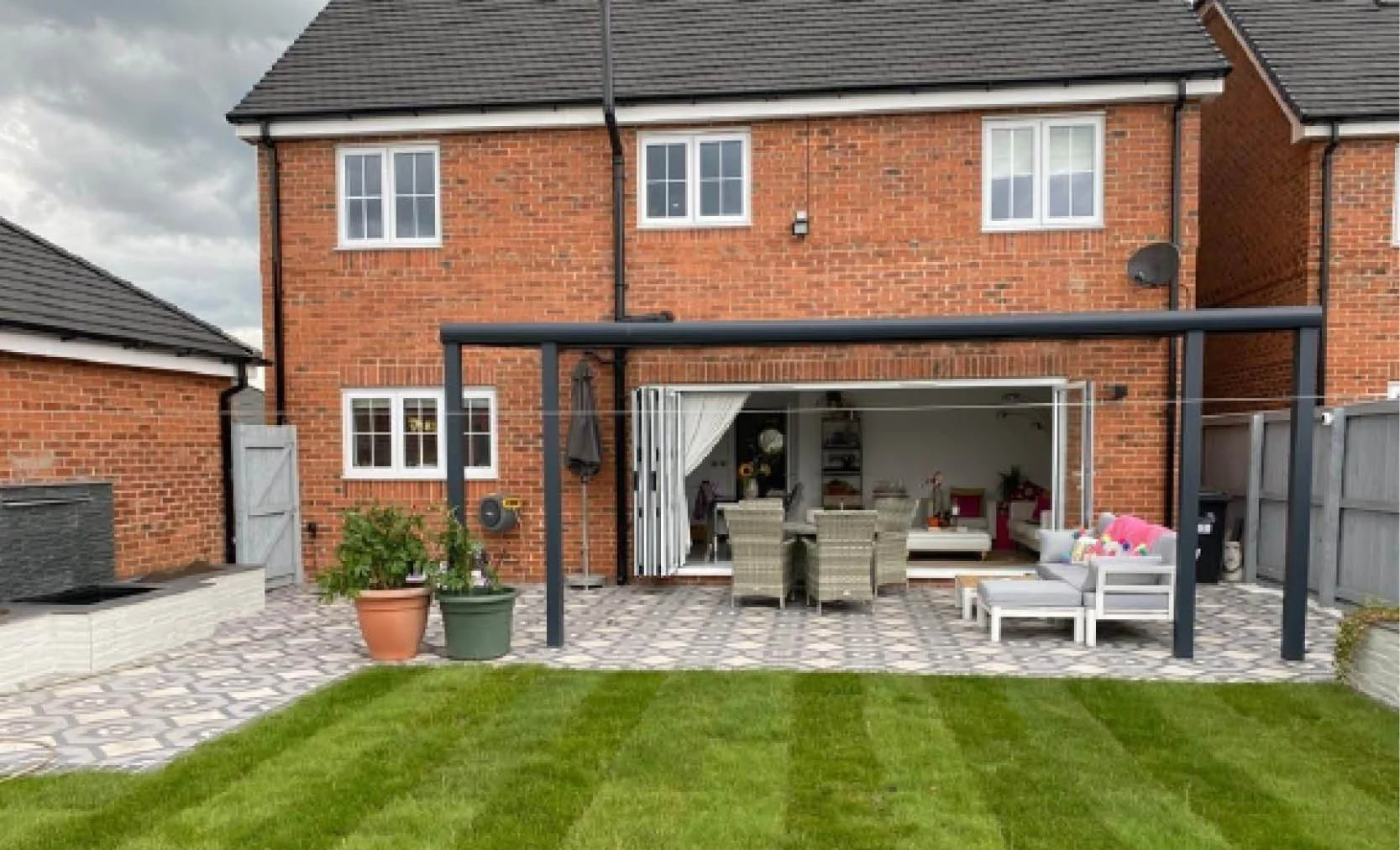 Backyard patio with outdoor furniture, potted plants, and a house with brick exterior and open sliding glass doors.