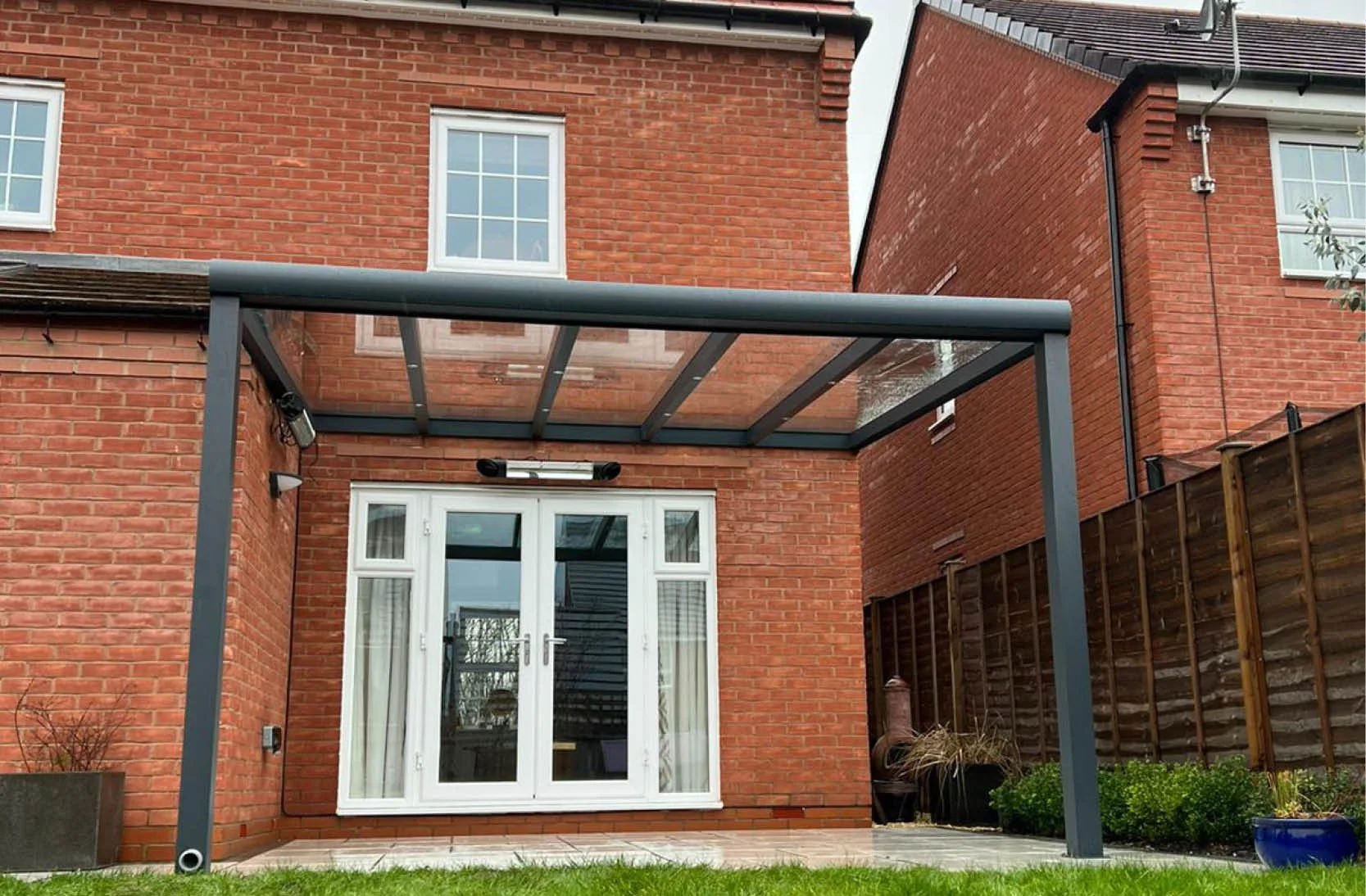 Backyard of a brick house with a patio, glass roof structure, and a white door with glass panes.