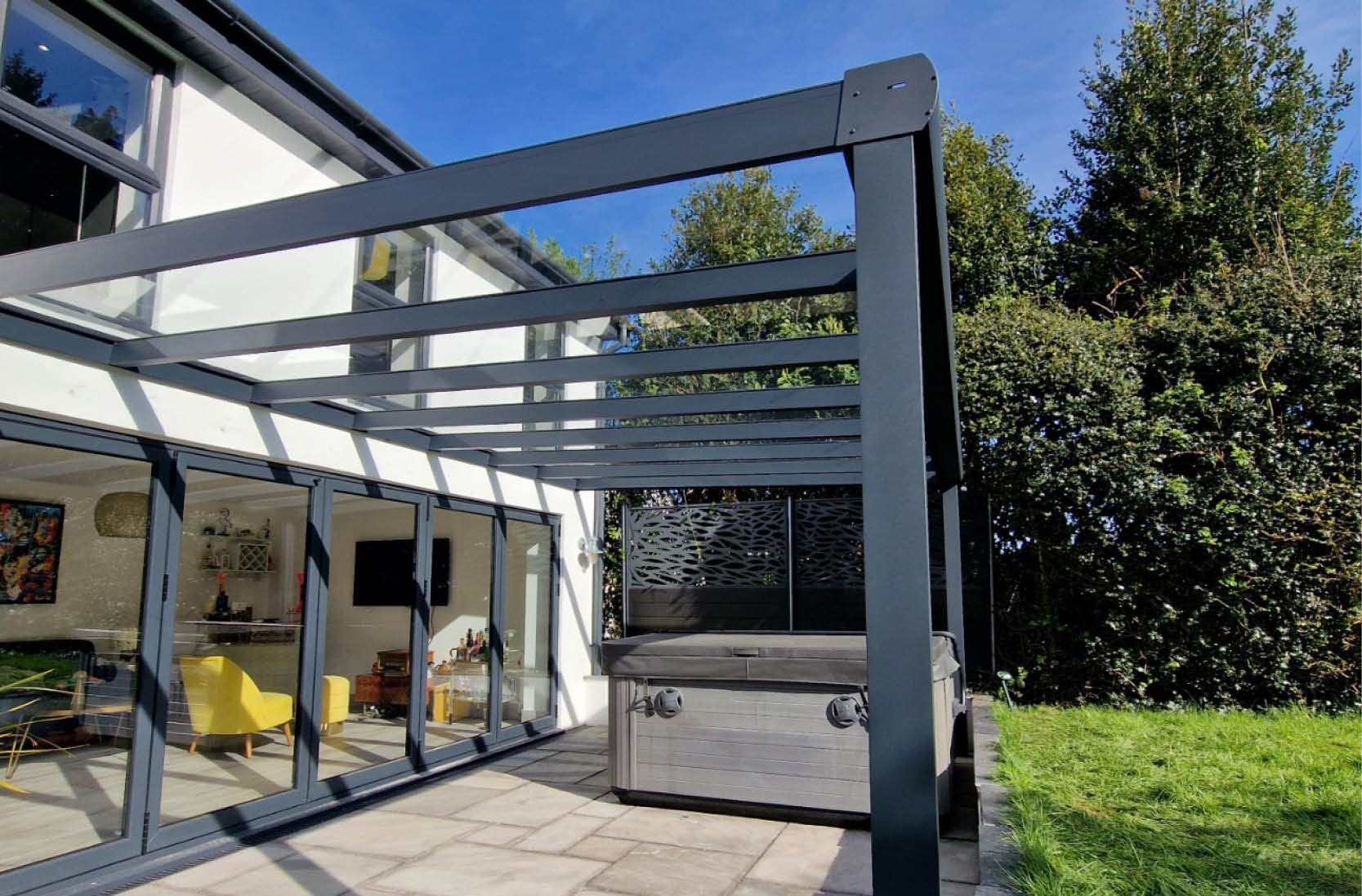 Back patio area with a glass-enclosed room and a metal framework for a future pergola or cover, grassy yard, and backyard trees.