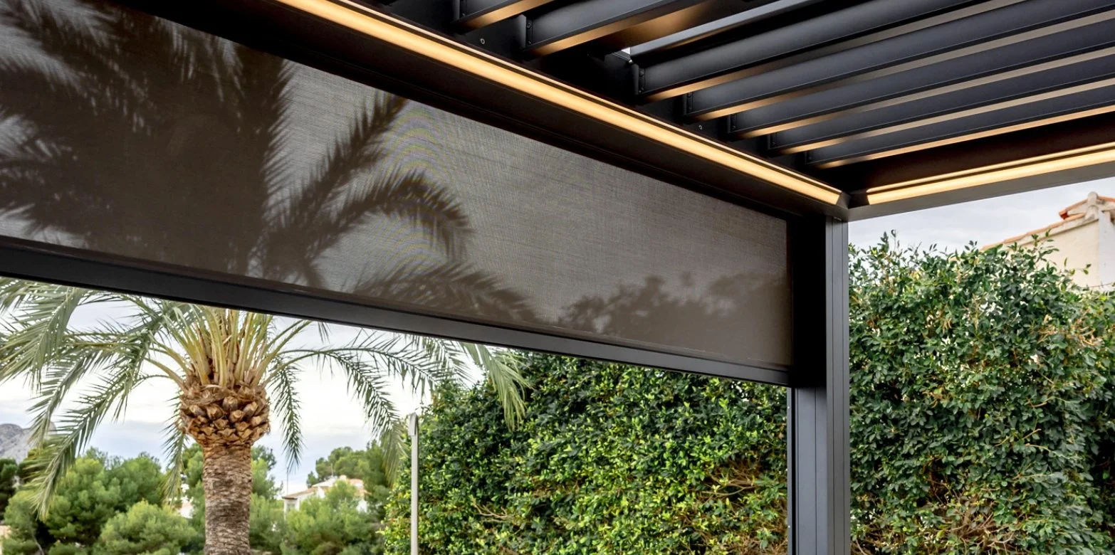 Outdoor patio area with a modern pergola with horizontal slats, surrounded by lush green trees and bushes, with a tall palm tree visible in the background.