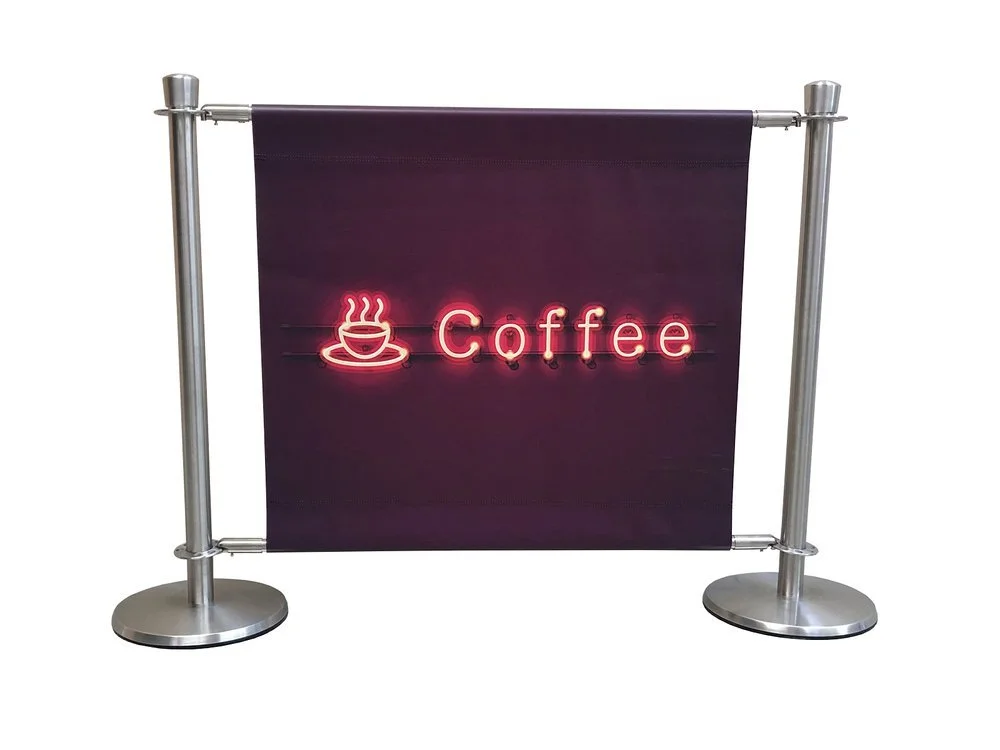 Neon sign with a steaming coffee cup icon and the word "Coffee" on a dark fabric background, supported by metal stanchions.