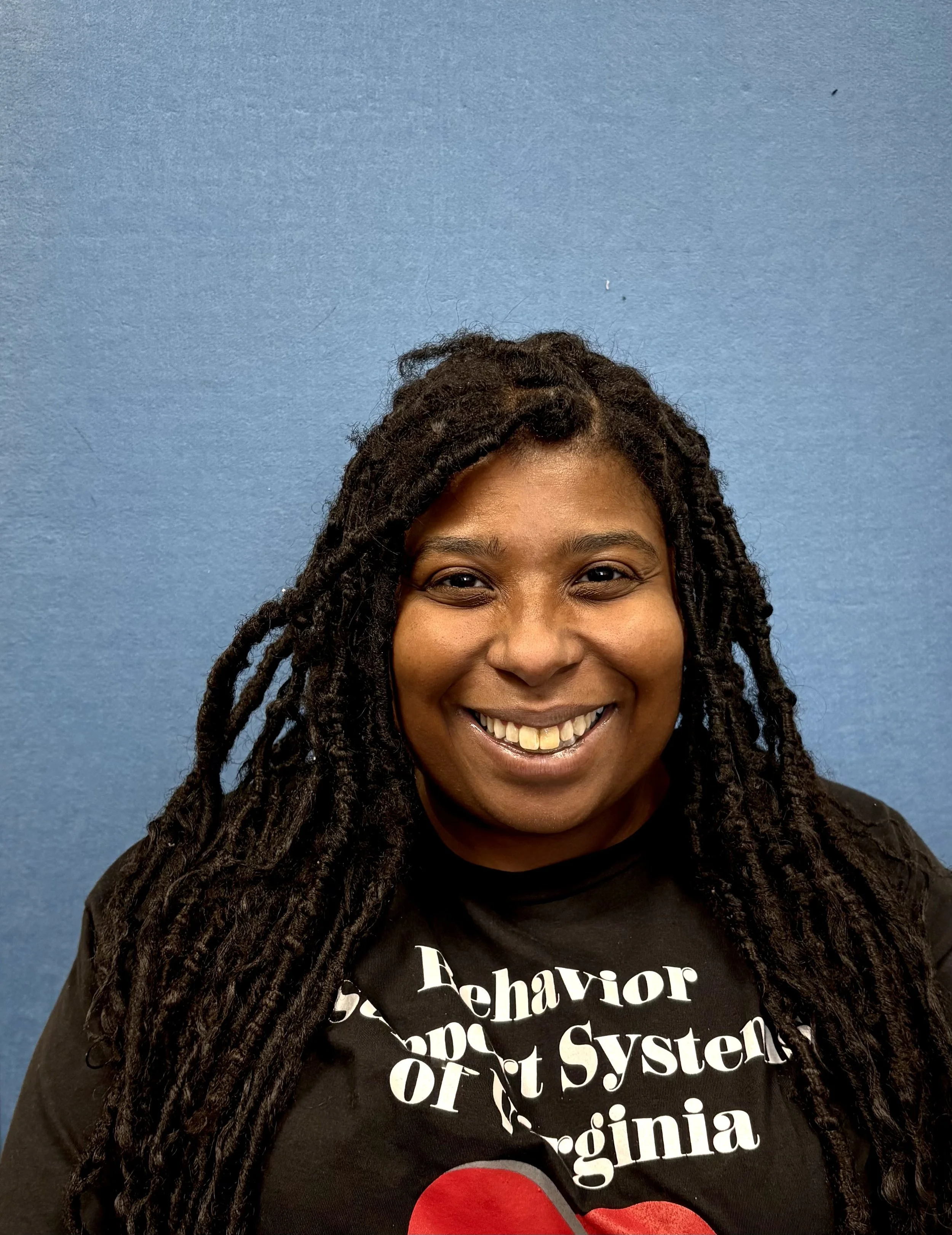 A person with glasses smiling in front of a blue background.