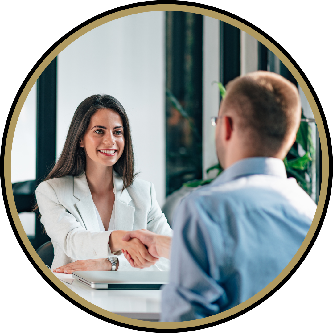 Une femme souriante en veste blanche serre la main d'un homme en chemise bleue lors d'un entretien d'embauche en intérieur près d'une fenêtre.