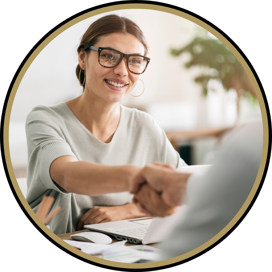Une femme souriante, portant des lunettes et des boucles d'oreilles en anneau, serre la main d'une autre personne dans un environnement lumineux.