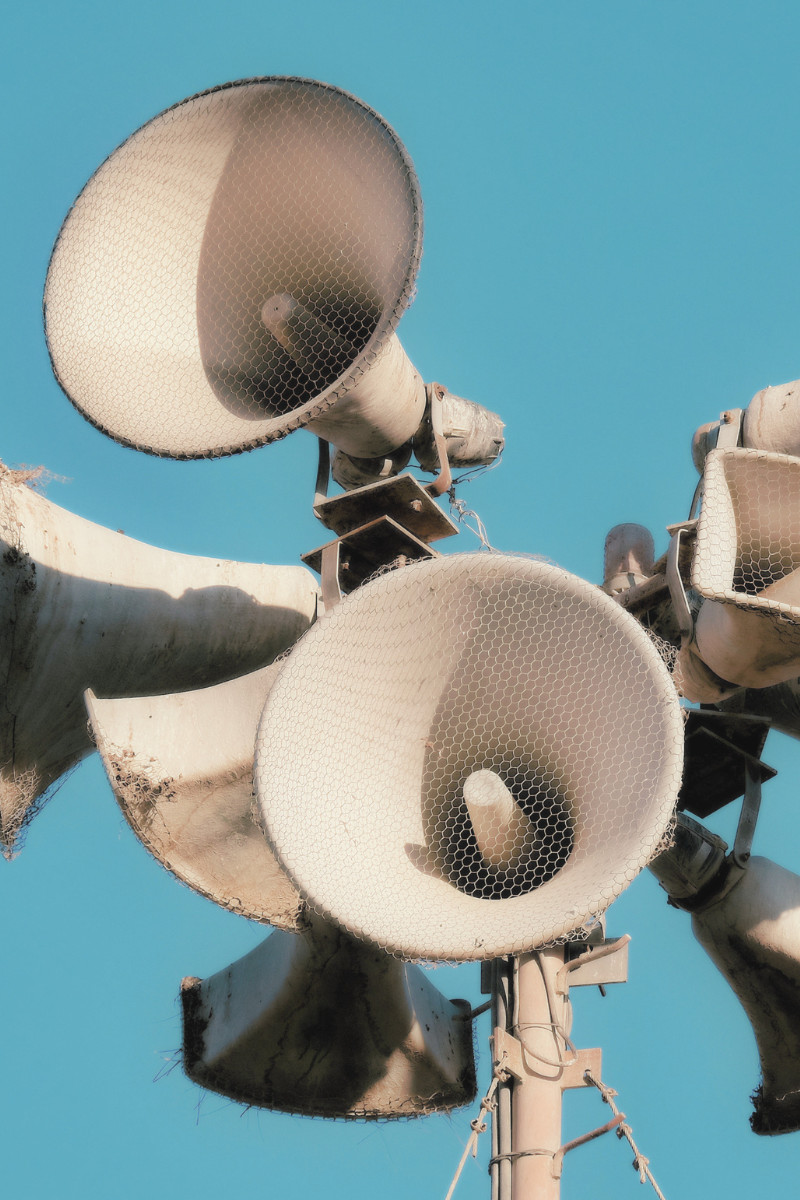 A cluster of white megaphones on a tall pole, with blue sky in the background