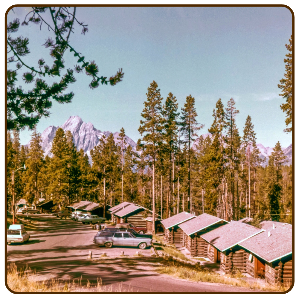 A 1970s image of cabins set in front of tall pines and a mountain range