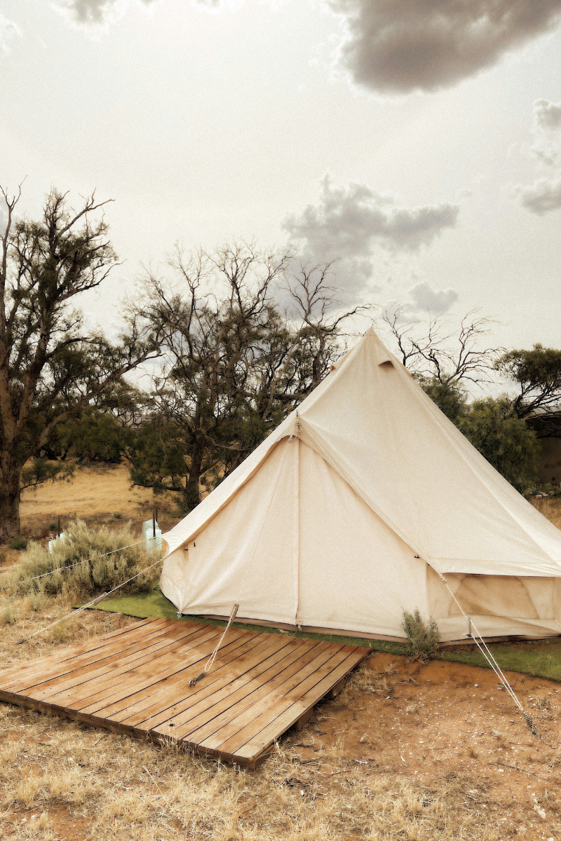 A canvas tent with a wooden platform in front of it, surrounded by scrubby trees