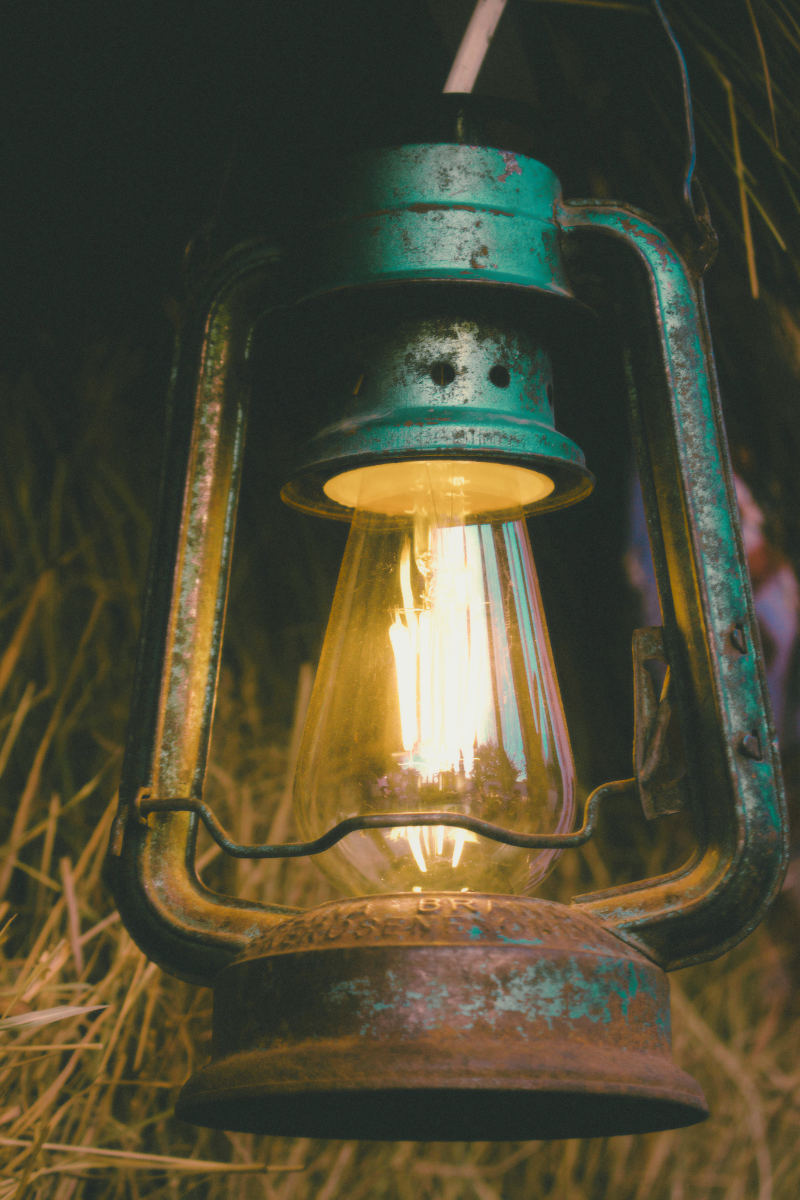 An old, green camping lantern with an edison bulb inside