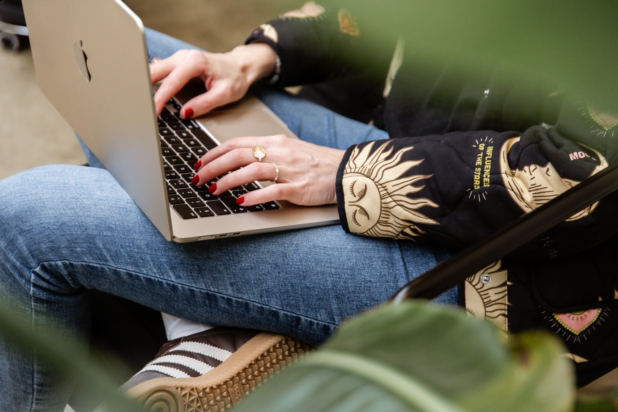 Person in Jeans arbeitet an einem Laptop, mit einer Jacke mit Sonnenmuster.
