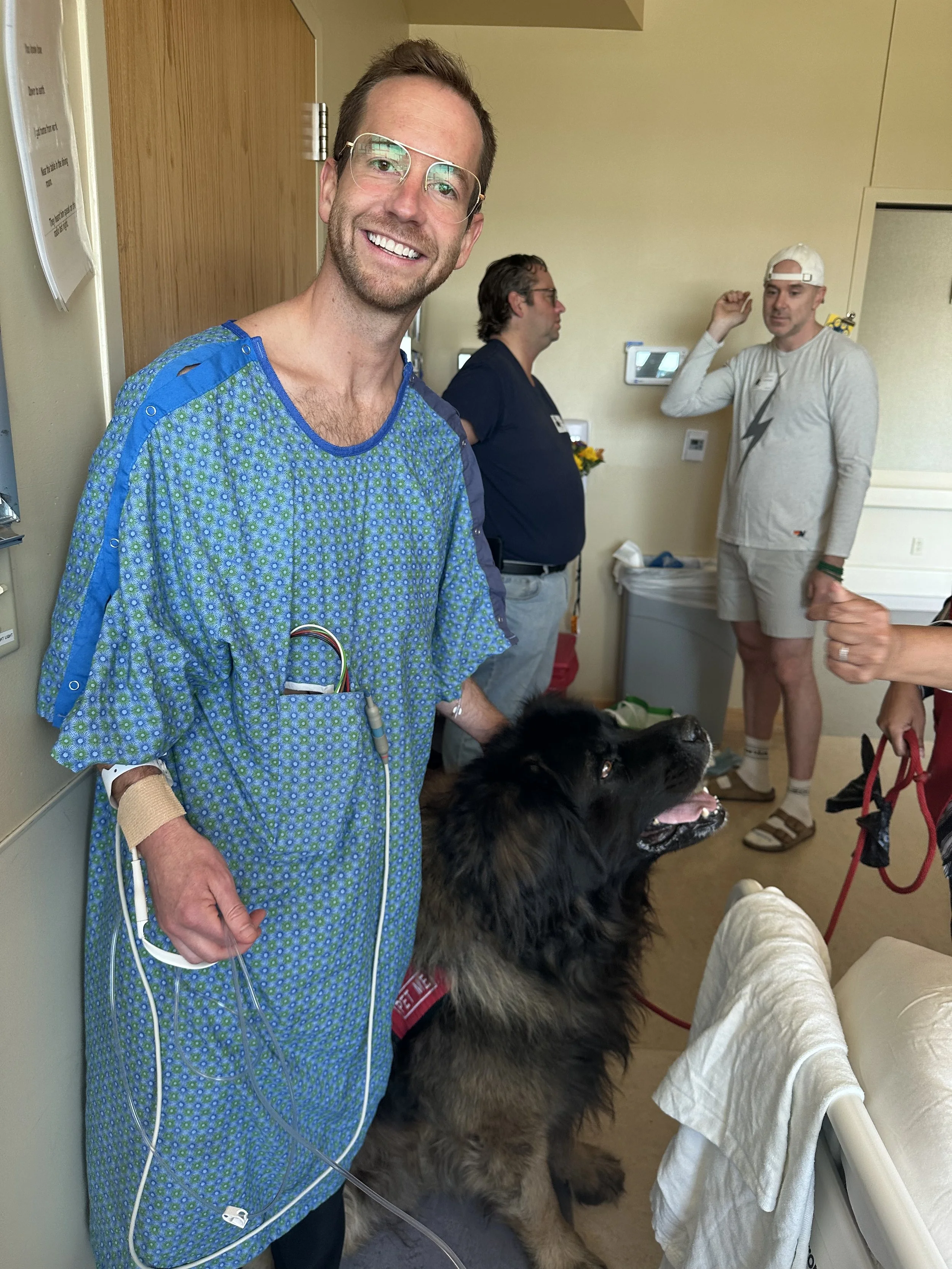 Man in hospital gown petting dog in hospital room