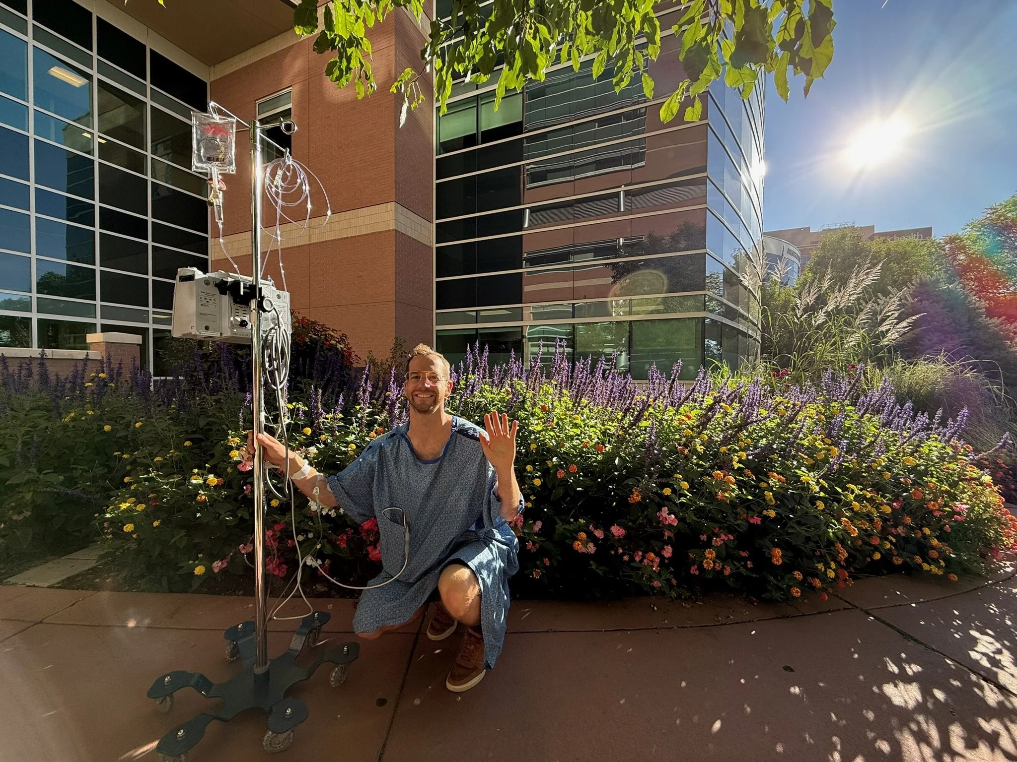 jake mcwink wearing a blue hospital gown kneeling in front of garden outside of hospital