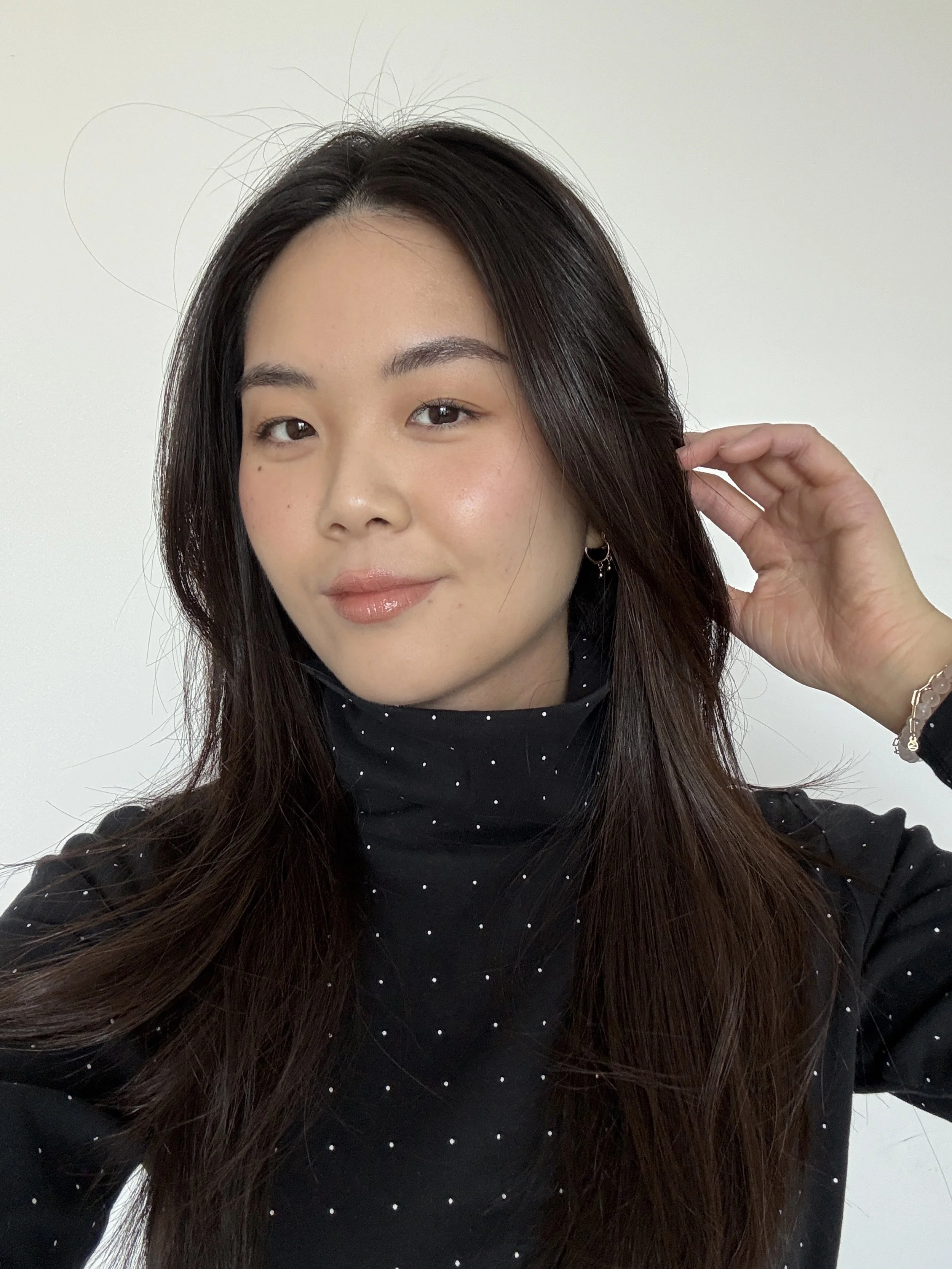 Asian woman with black hair and natural brows smiling in front of white background.