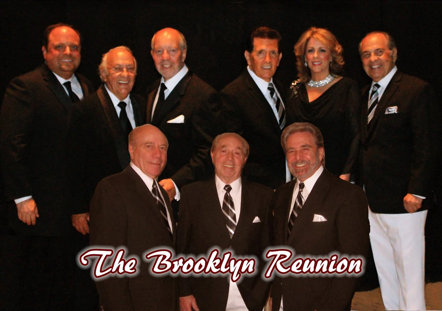 Group of ten people dressed in formal black tuxedos, standing against a dark background. Text overlay reads 'The Brooklyn Reunion' in red cursive font.