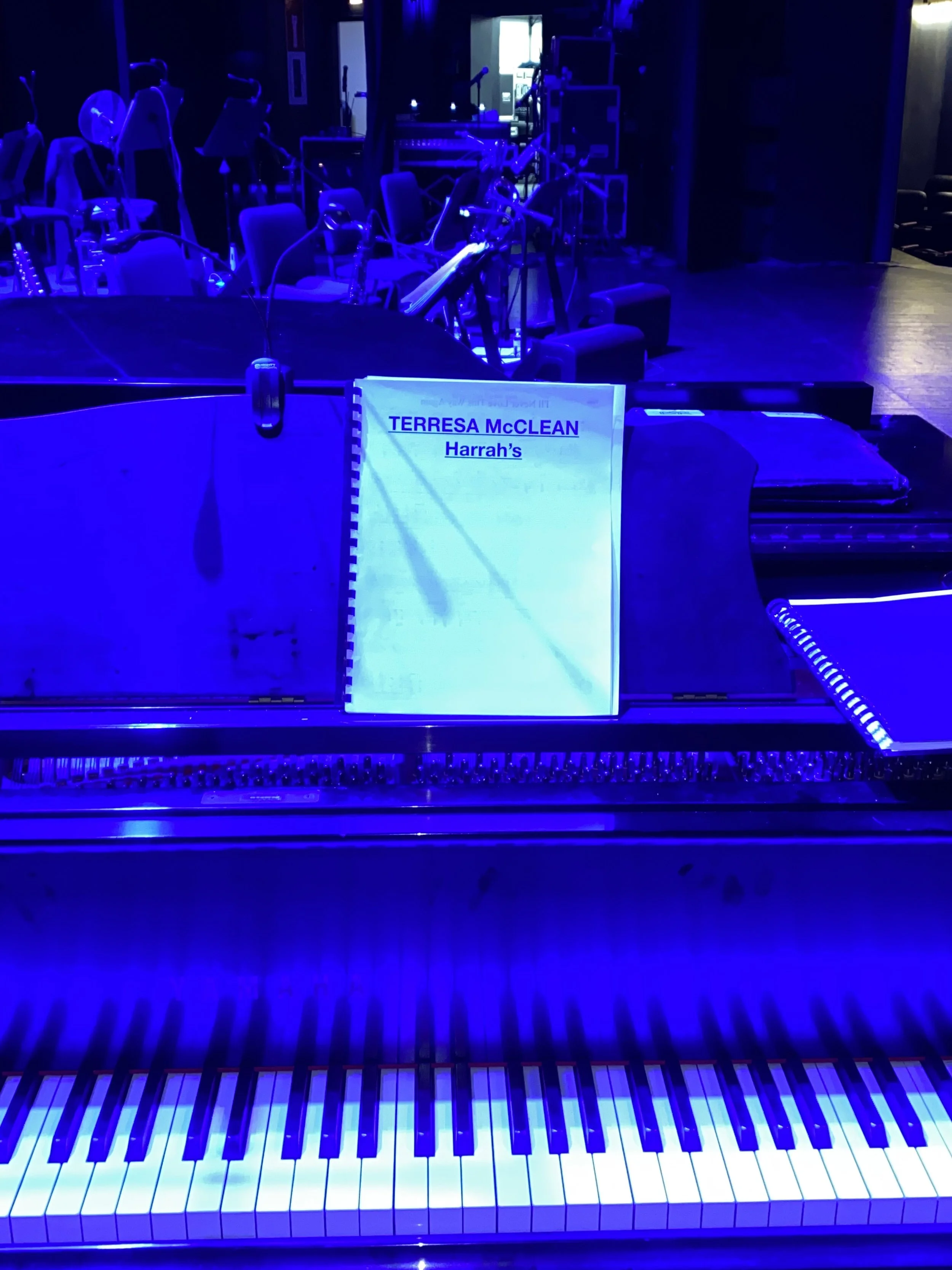 A blue-lit piano with a music sheet titled 'TERESA McCLEAN Harrah's' on the music stand.