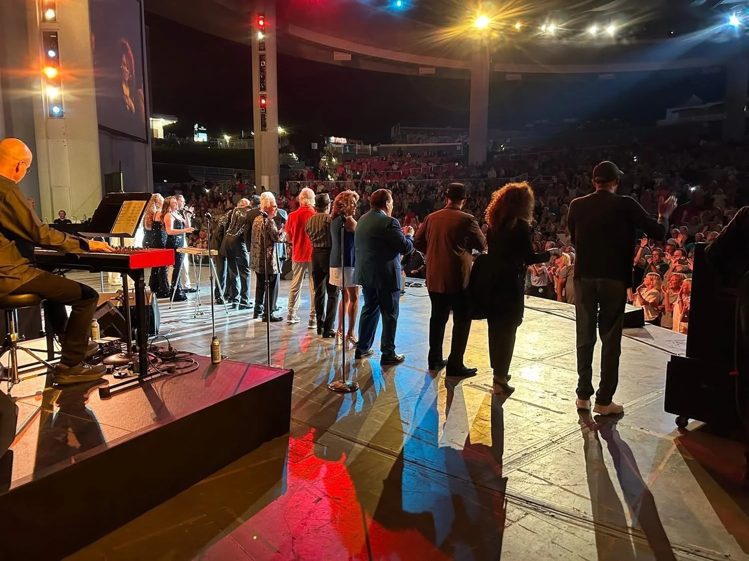 Musicians and performers on stage during a concert or show, with a large audience in the background.