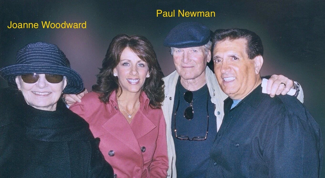 Group of four people posing together, two men and two women, smiling, with a dark background.