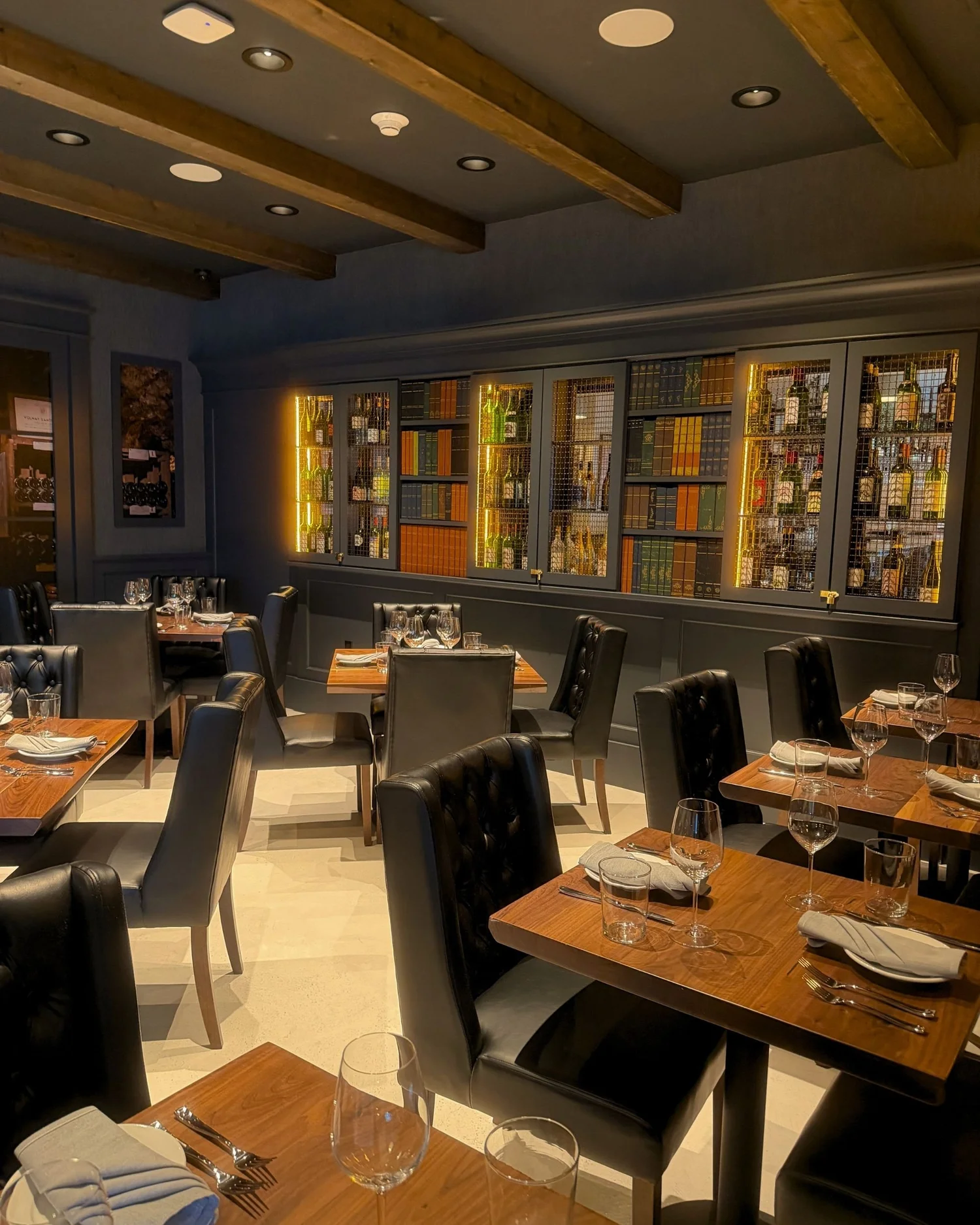 The Enology dining room with wooden tables and a wall of glass-fronted shelves