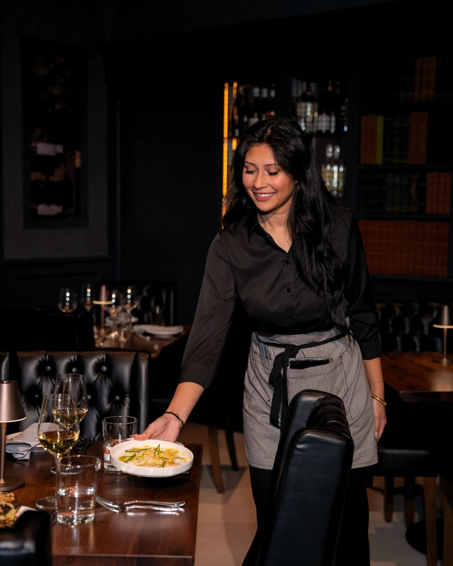A server tending a table in the dimly lit dining room at Enology