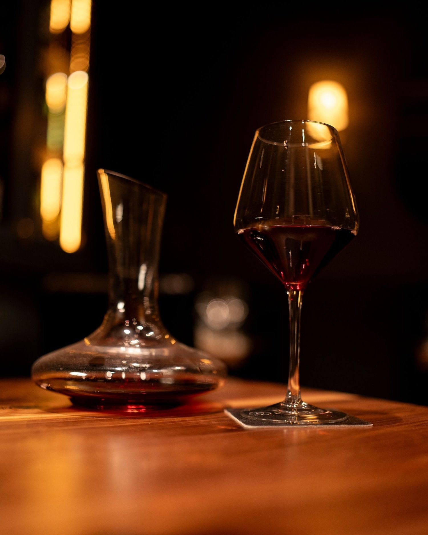 A glass of red wine resting on a wooden bar in warm light