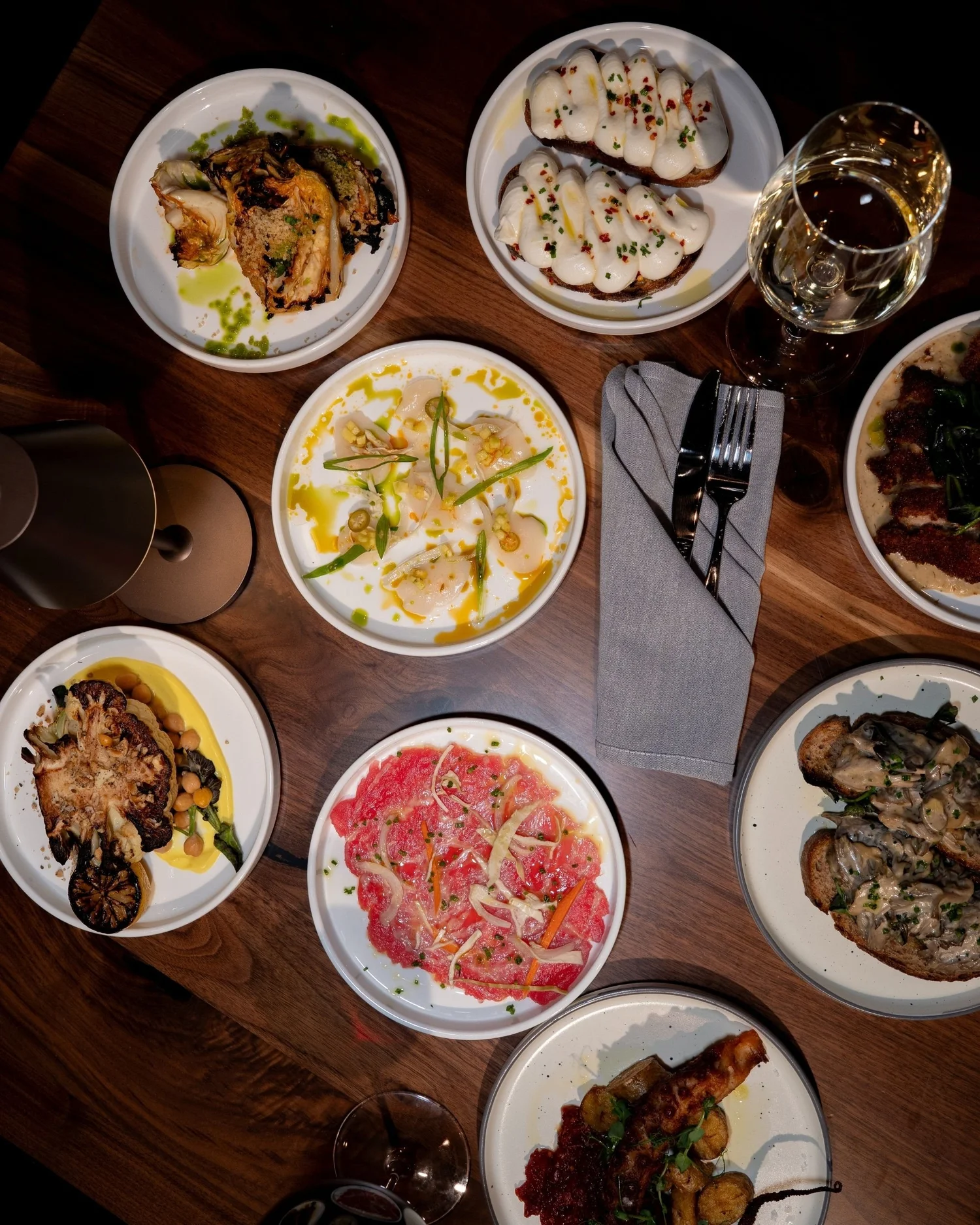 A spread of small plates on a wooden table, with roasted vegetables, bread, and cheese