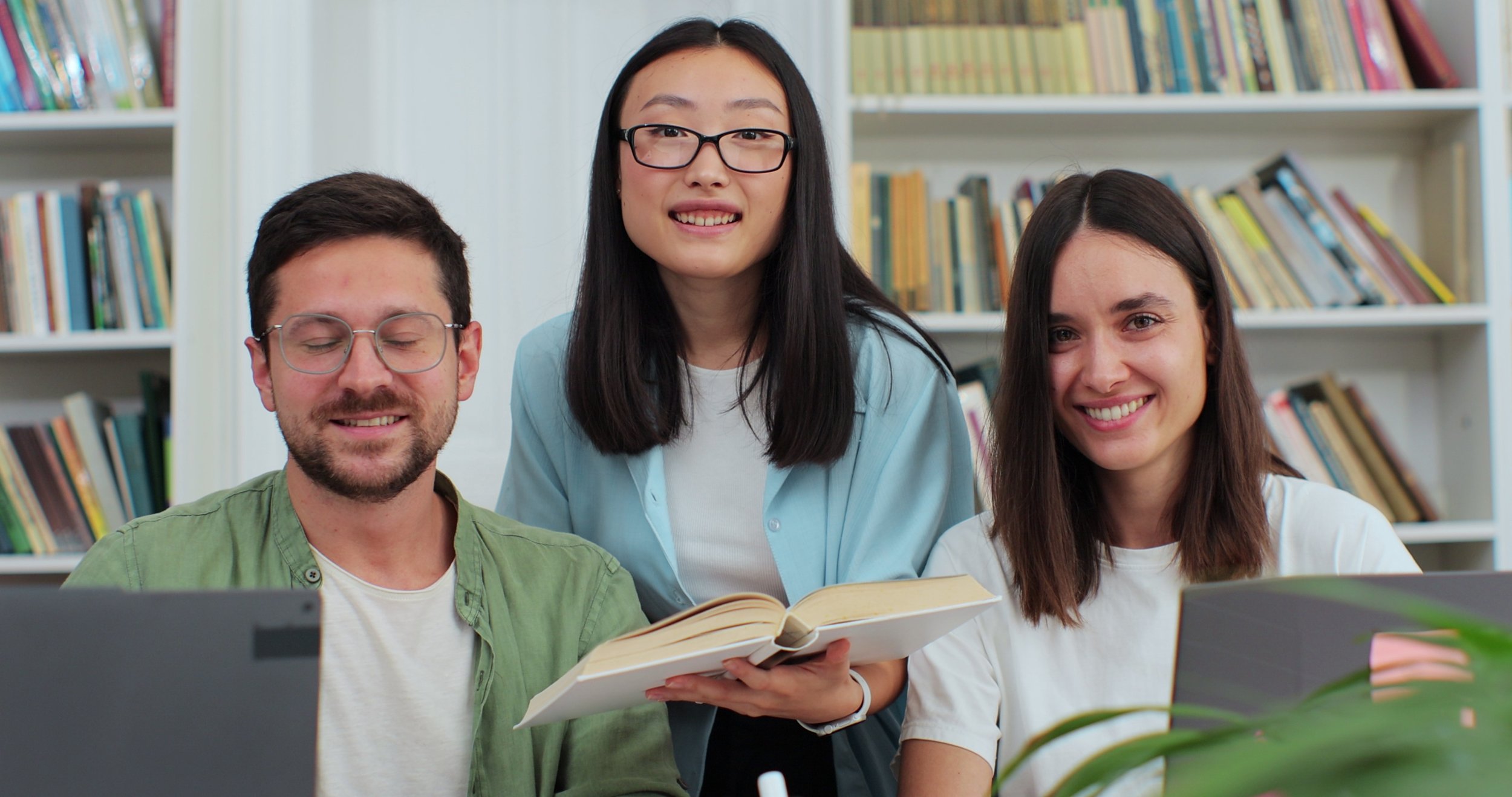 Three students smiling with a book