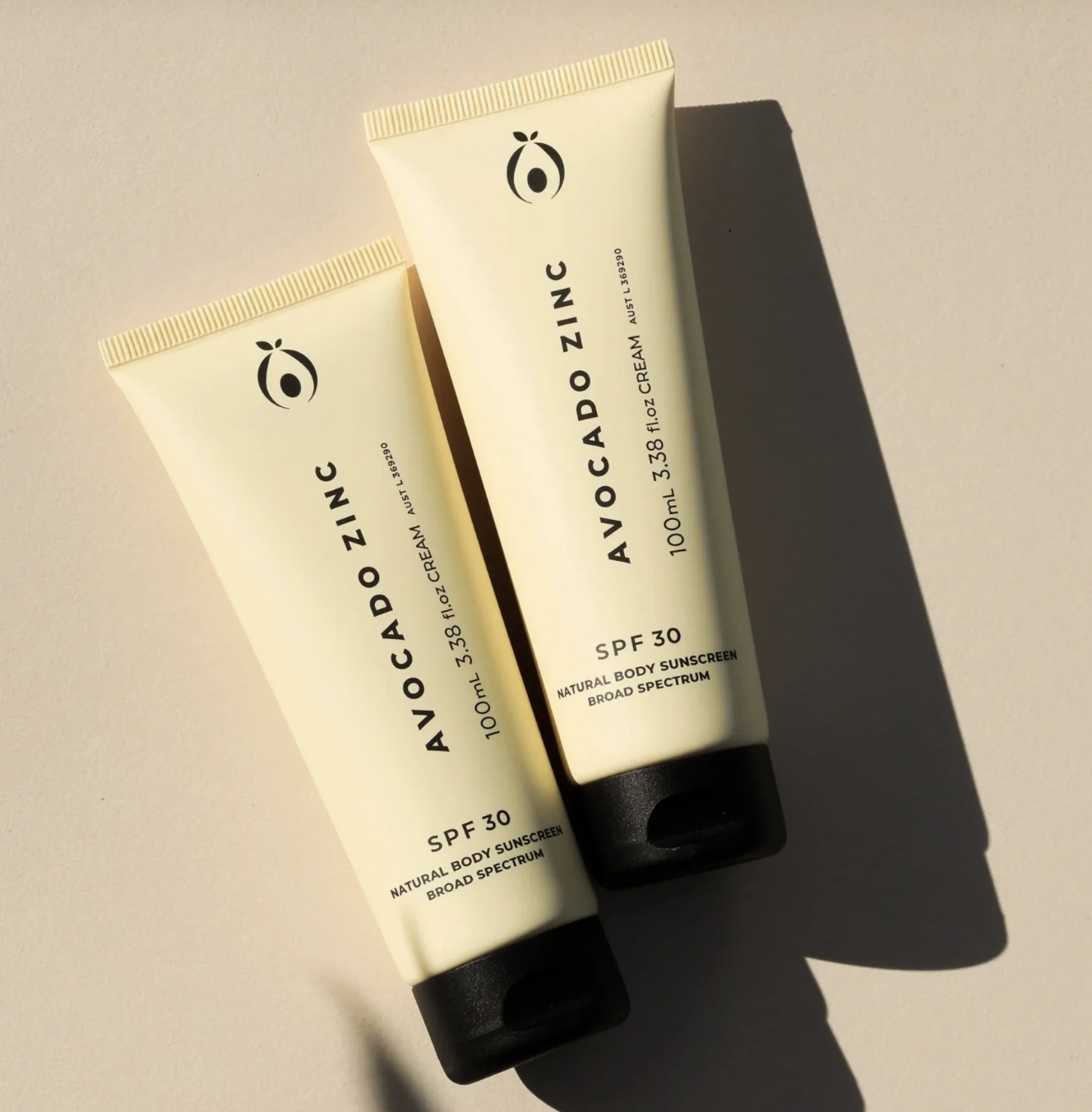 Two tubes of Avocado Zinc SPF 30 natural body sunscreen with broad spectrum, 100ml each, placed on a light-colored surface casting shadows.